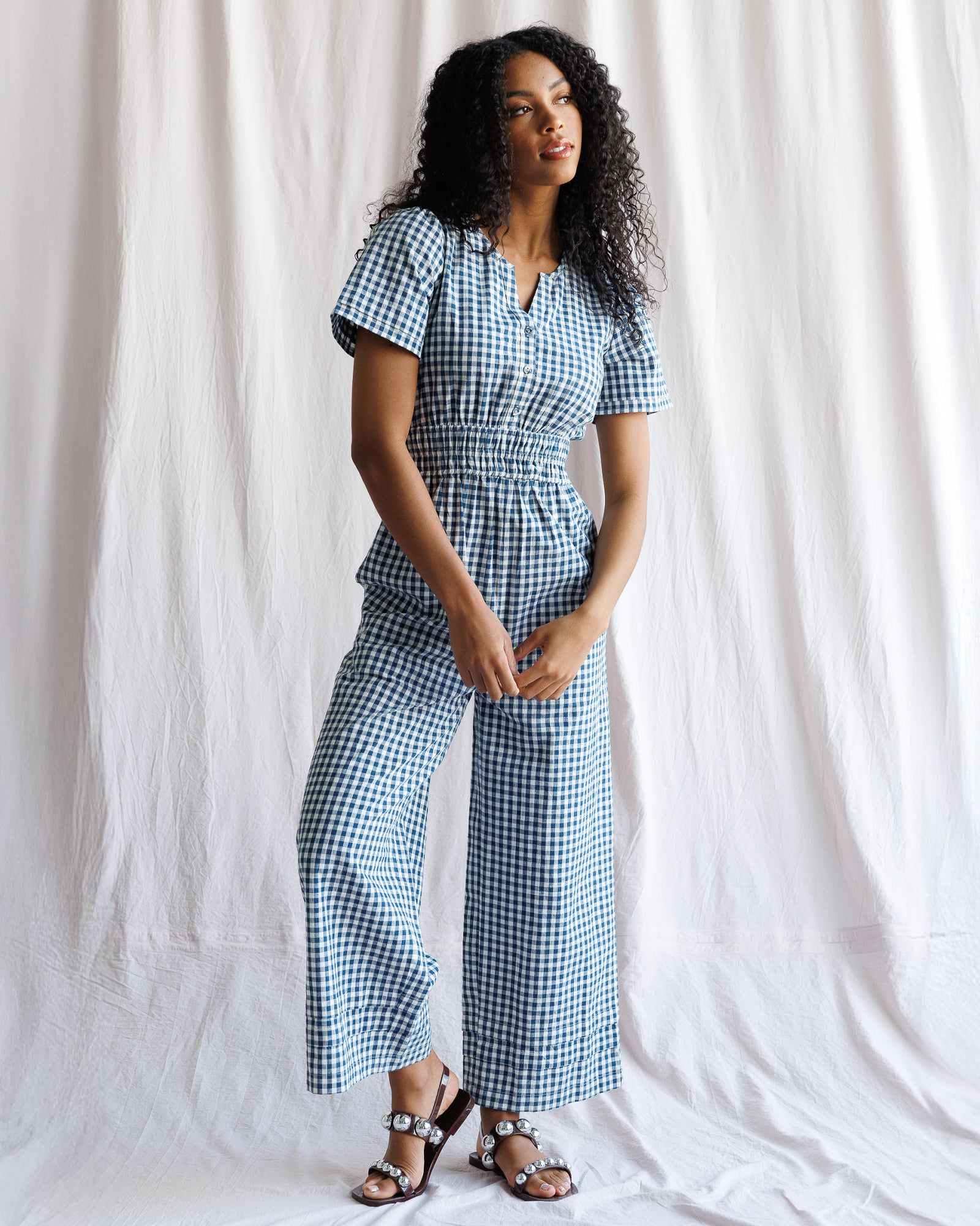 Woman wearing a blue and white checkered jumpsuit against a white background