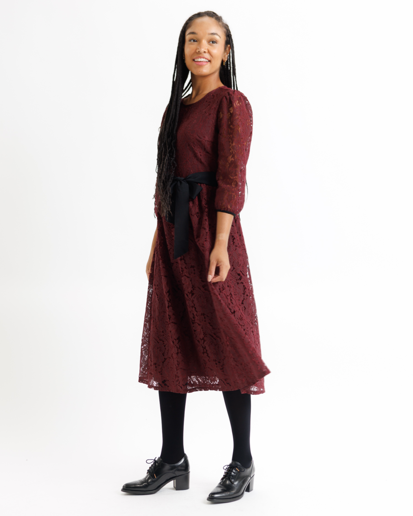Woman wearing a burgundy lace dress with a black satin bow on a white background