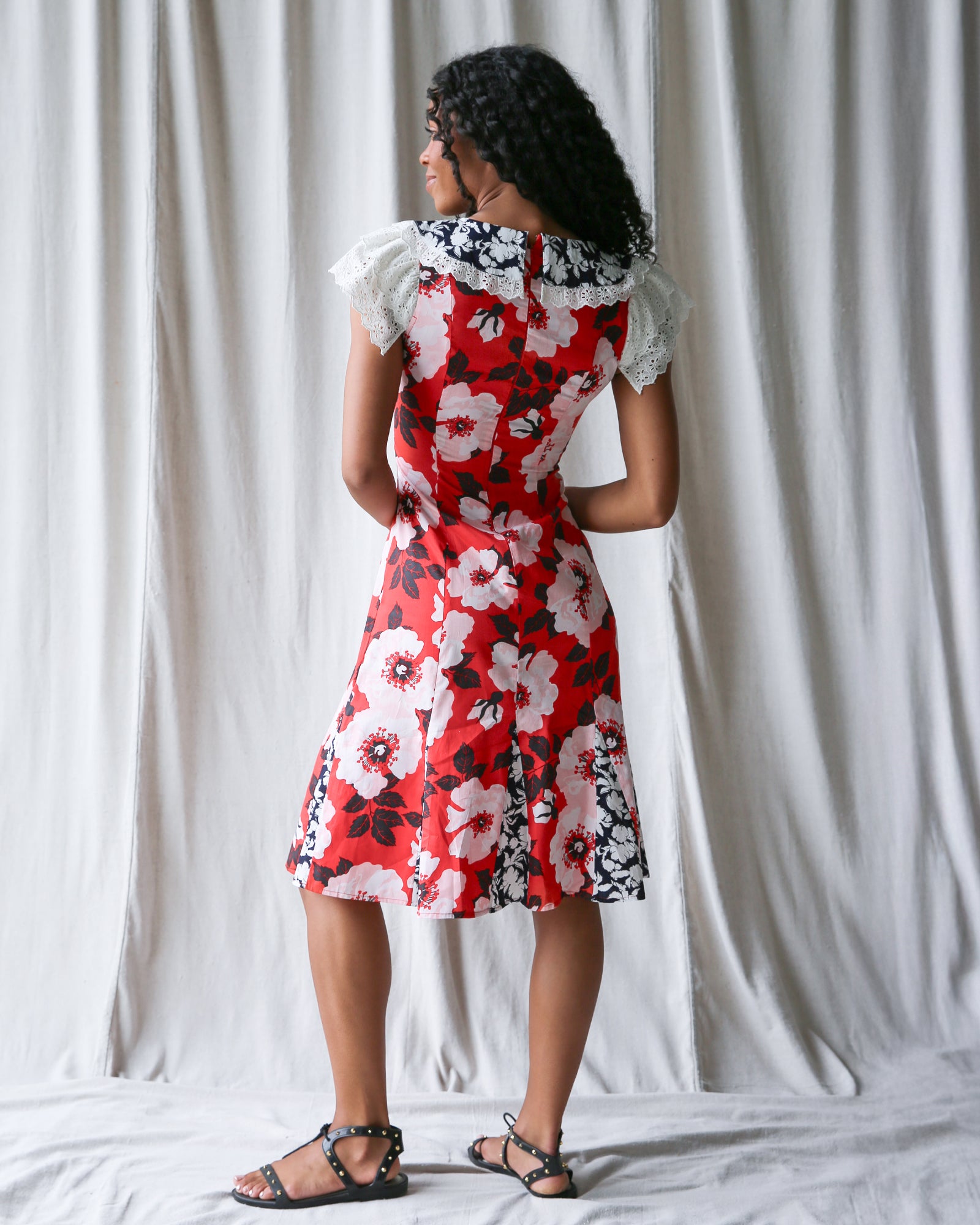 Woman wearing a red floral dress with white ruffled sleeves against a white curtain background