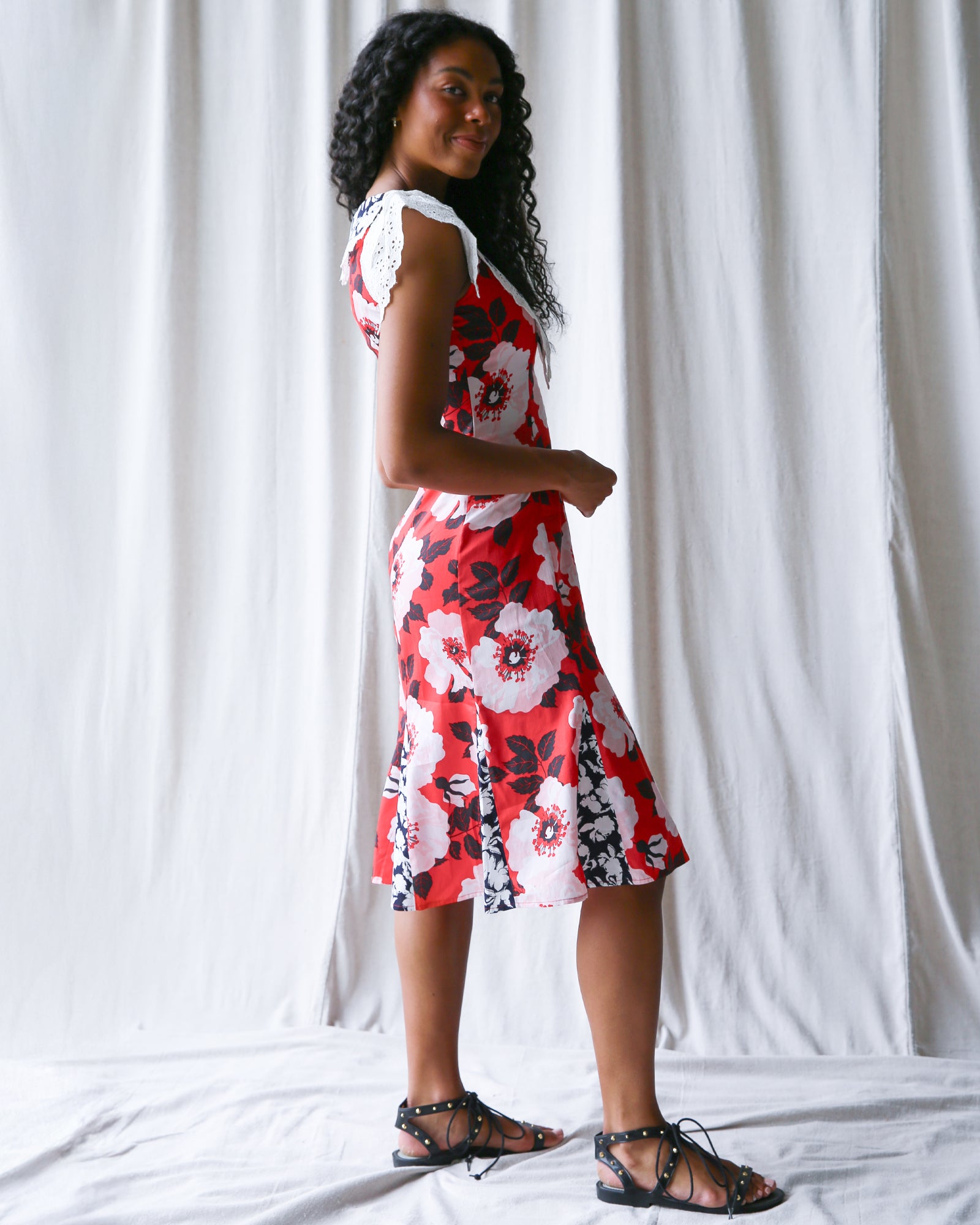 Woman wearing a red floral dress standing against a white curtain.