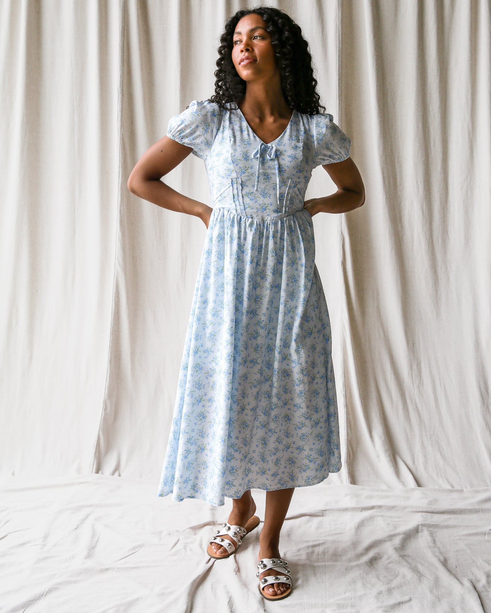 Woman wearing a light blue floral dress against a white curtain background