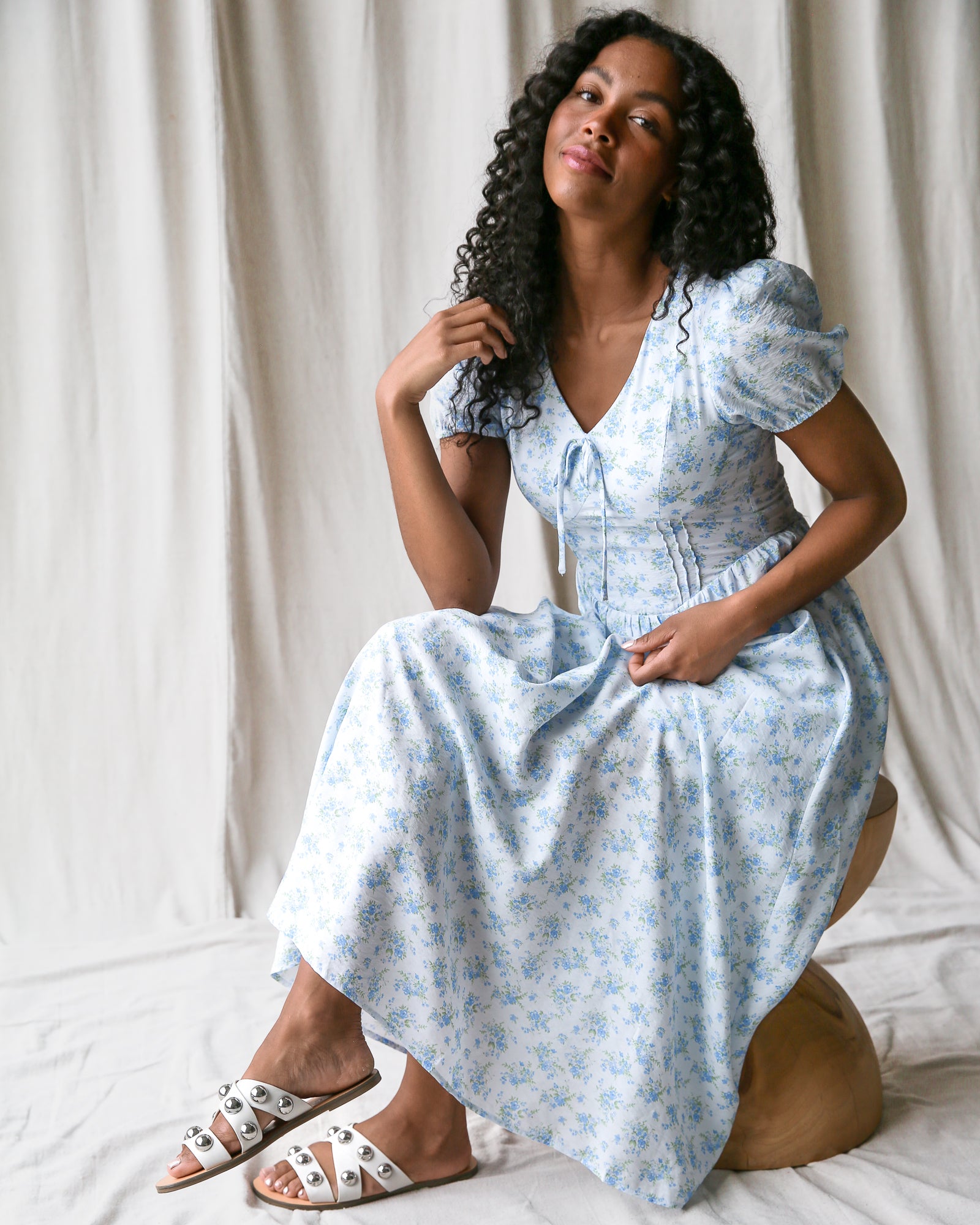 Woman wearing a light blue floral dress sitting on a white surface with a neutral background