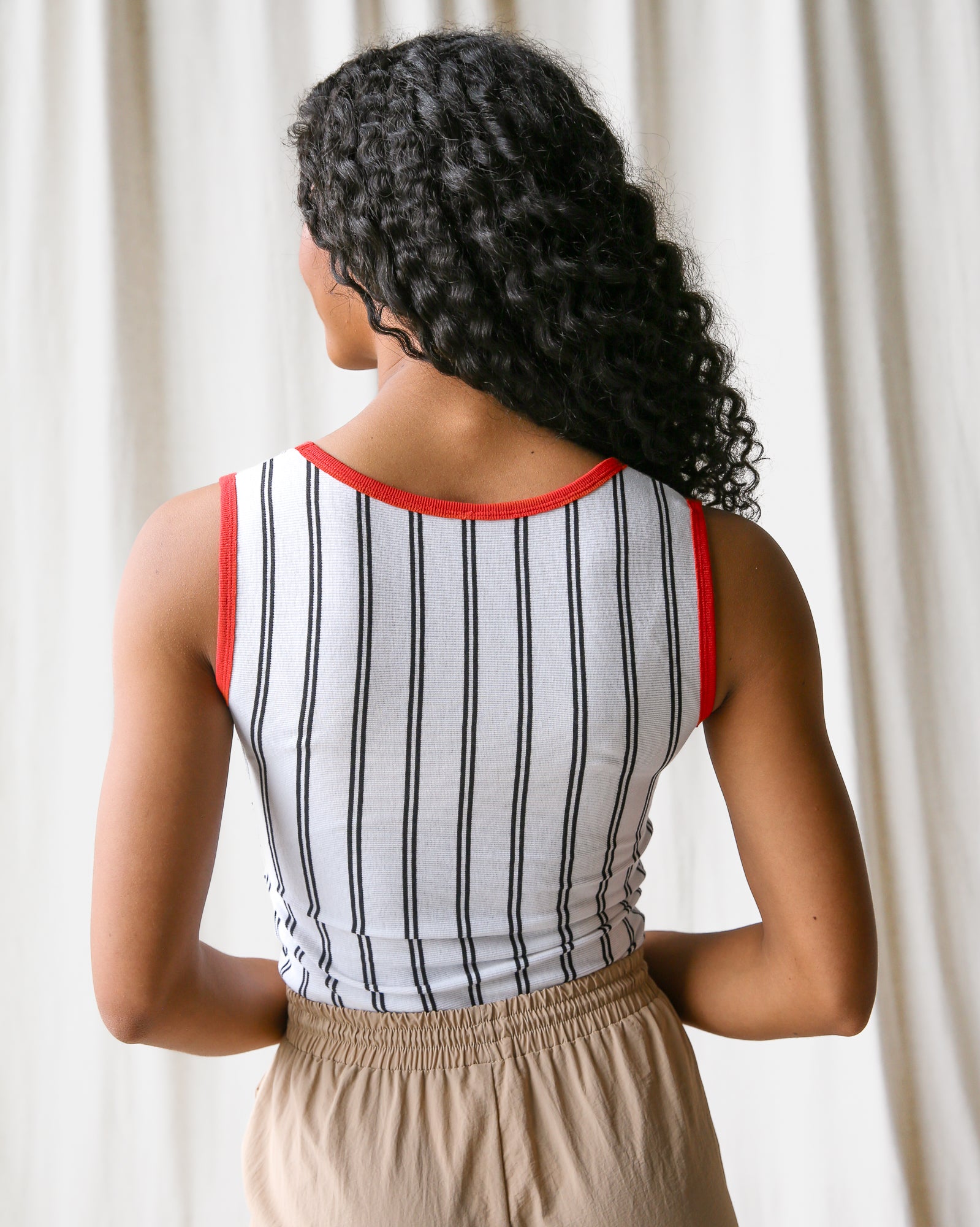 Woman wearing a striped tank top with red trim against a white curtain background