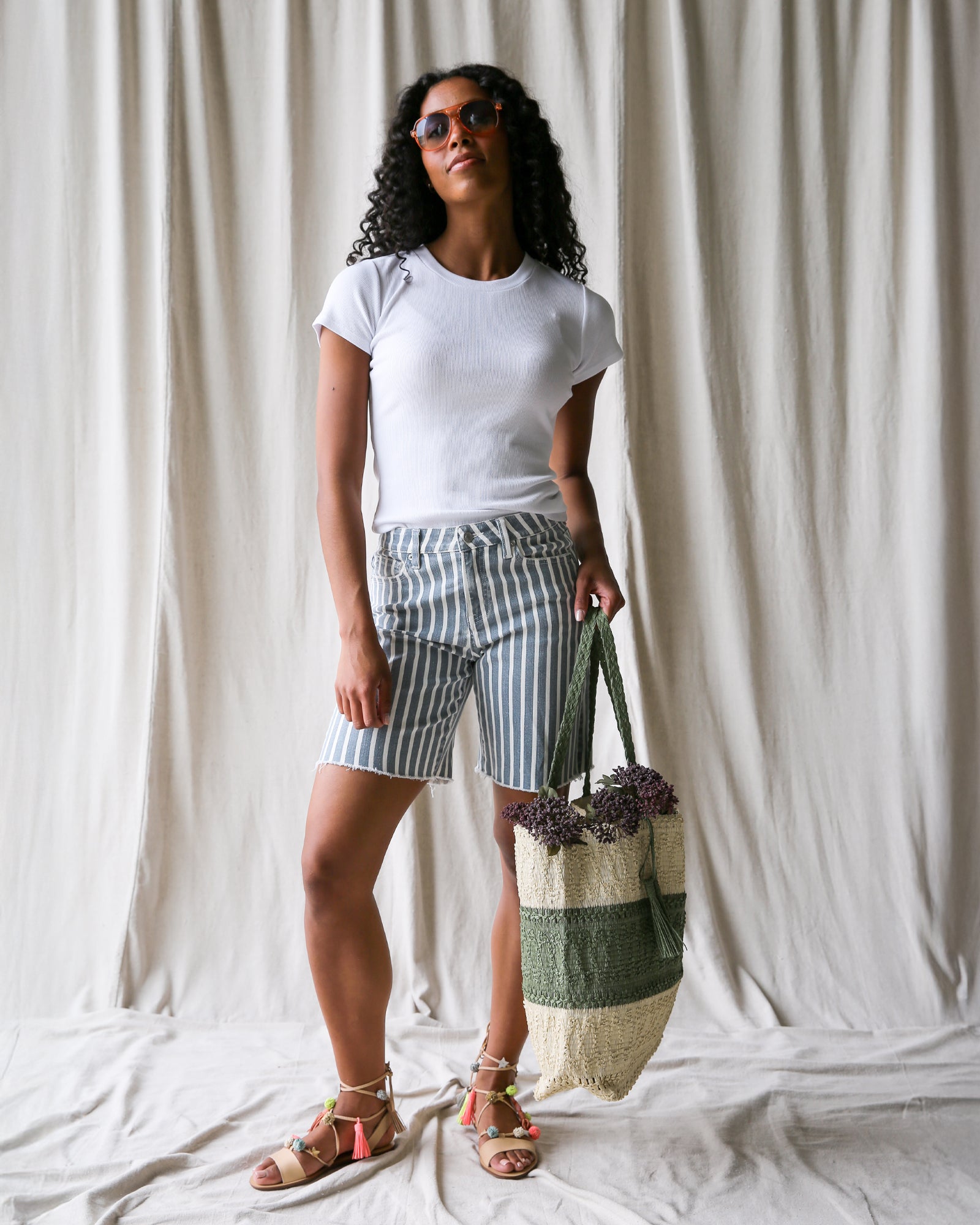 Woman holding a striped bag against a white curtain background