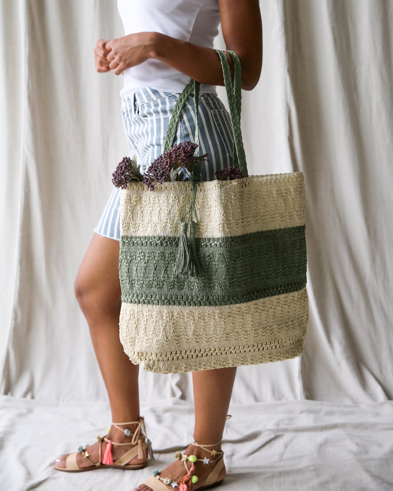 Green and beige woven tote being held by a woman