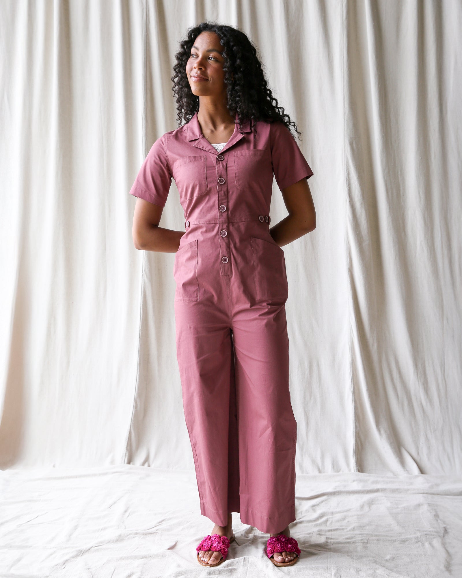 Woman wearing a pink outfit standing against a white curtain background