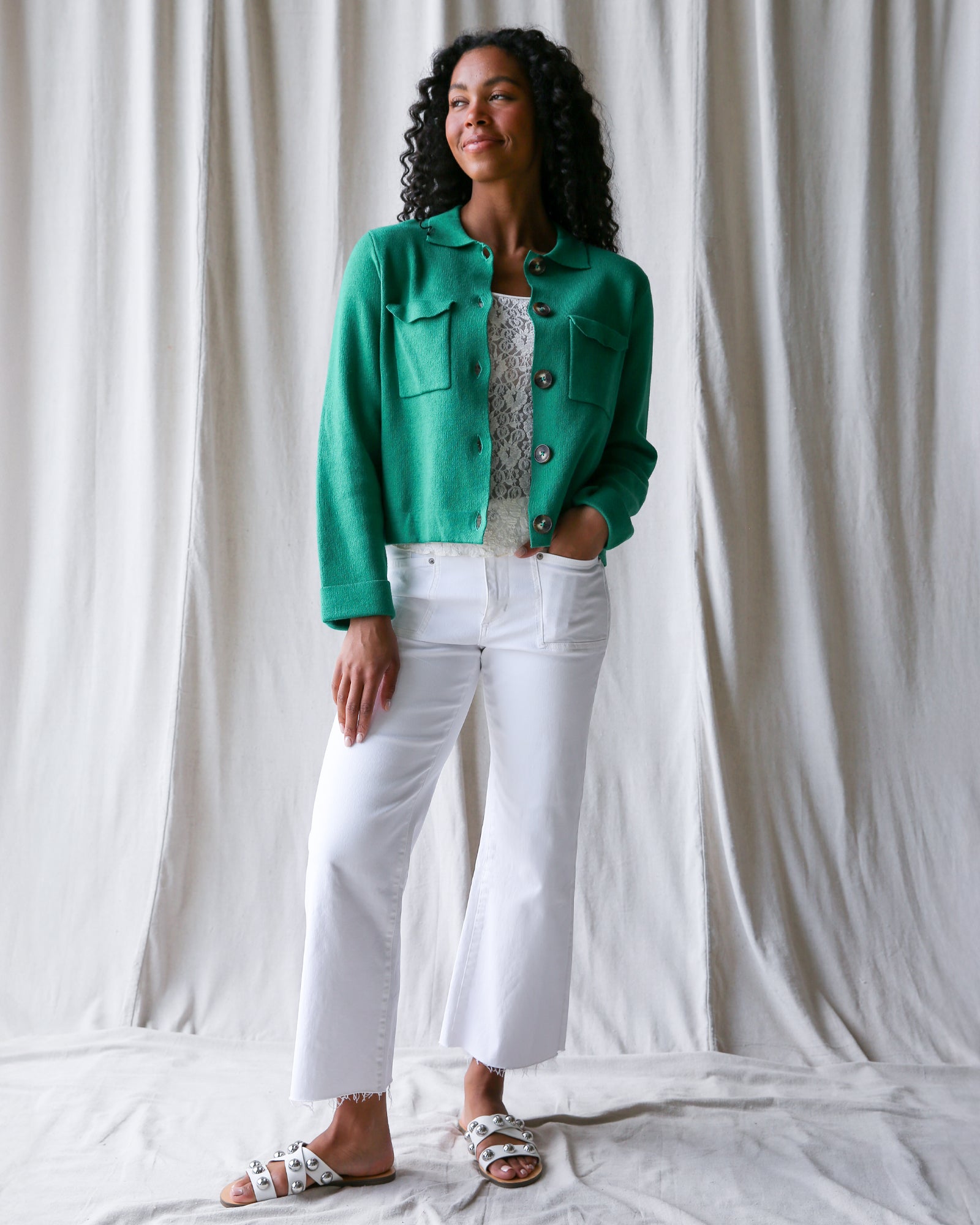 Woman wearing a green jacket and white pants against a plain background