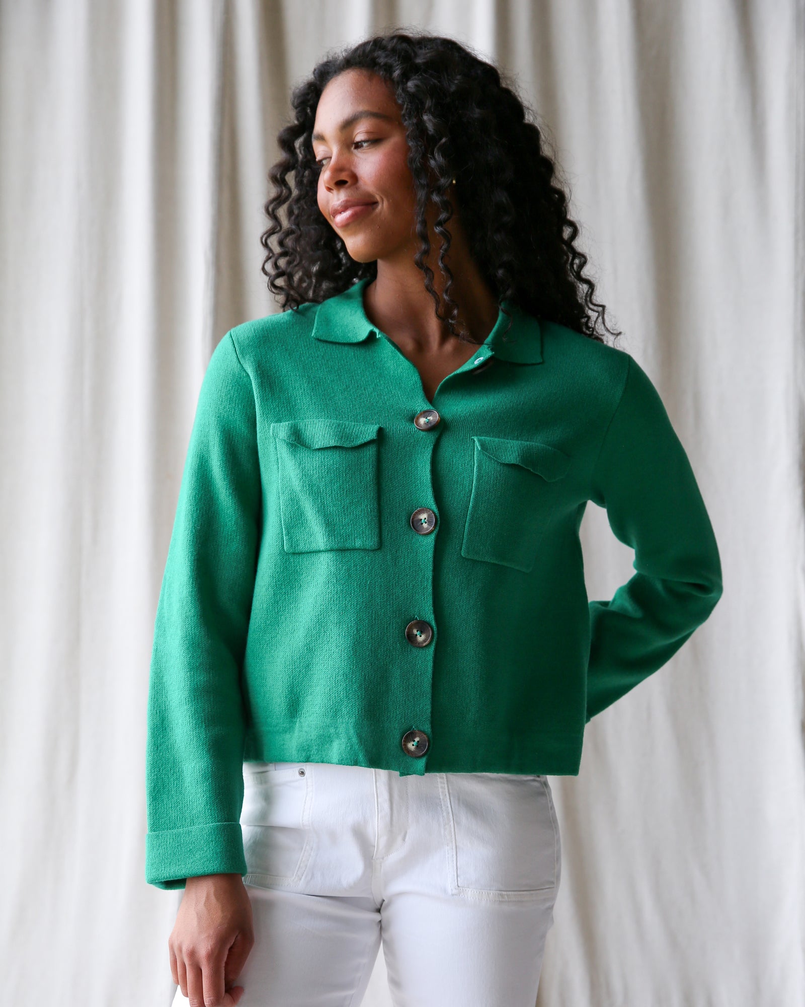 Woman wearing a green jacket with white pants against a neutral background