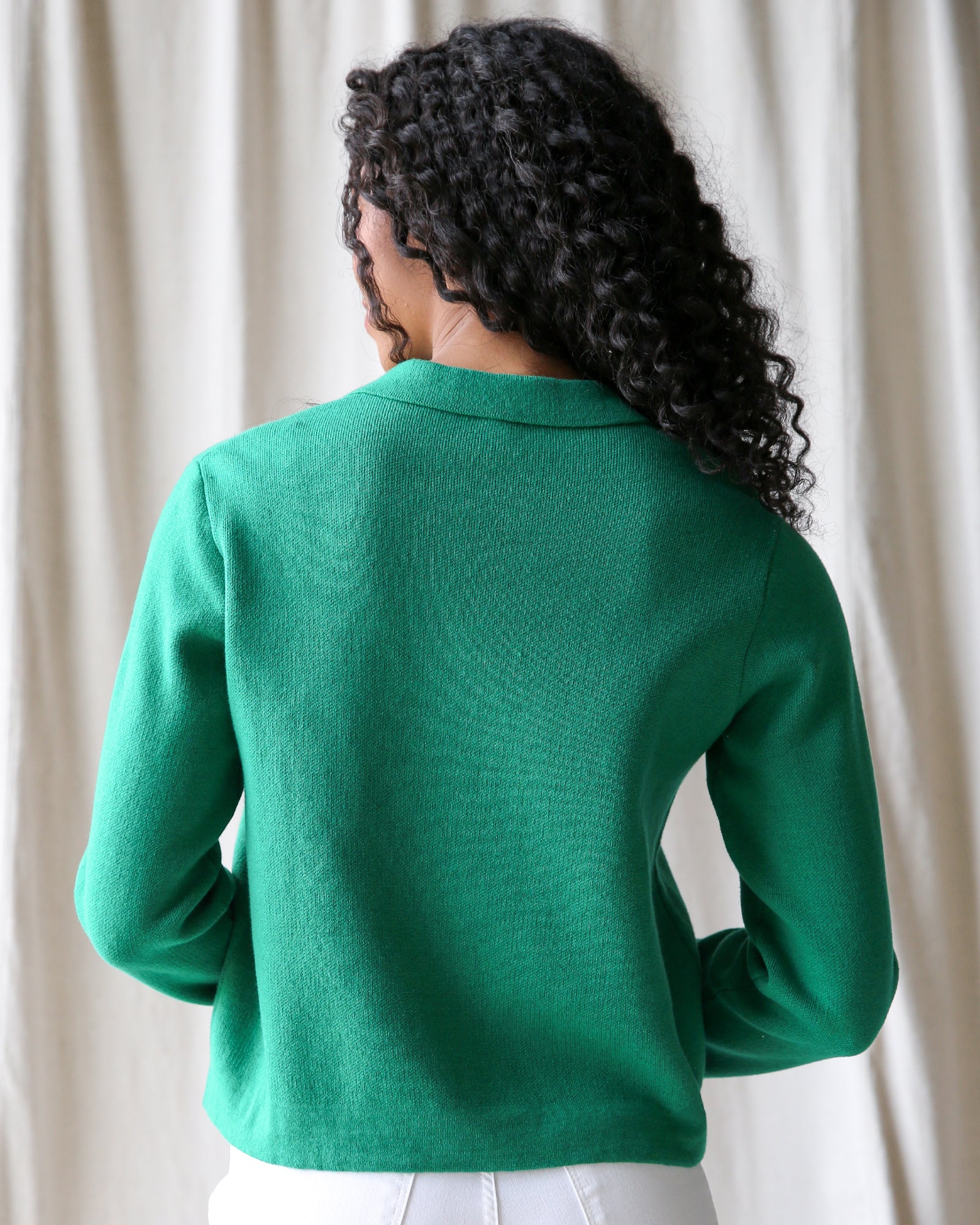 Person wearing a green blazer against a white curtain background