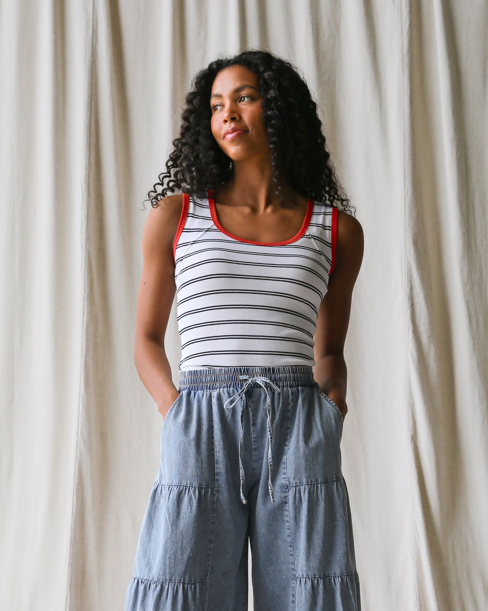 Woman wearing a striped tank top and denim pants against a plain background