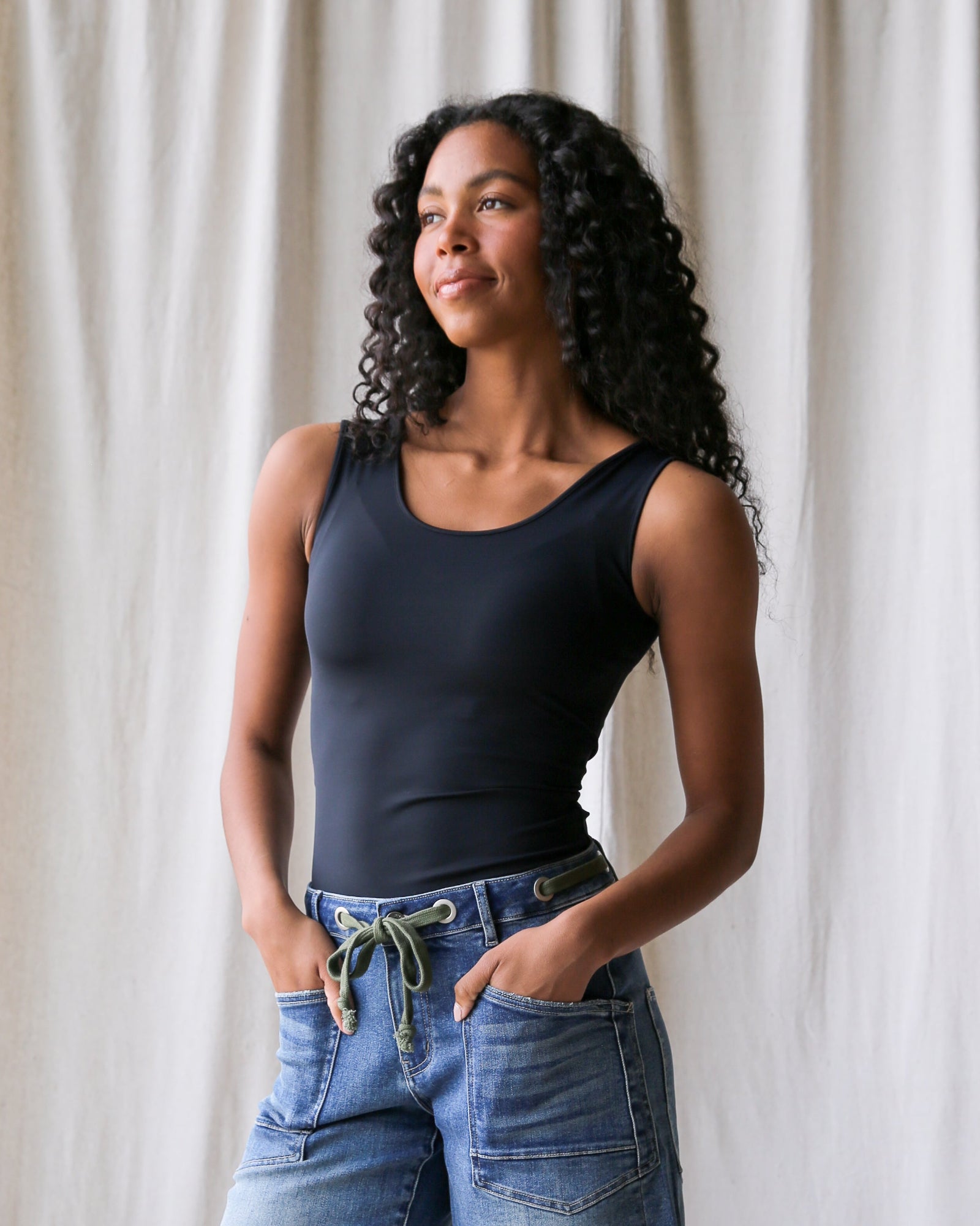 Woman wearing a black tank top and denim shorts against a plain background