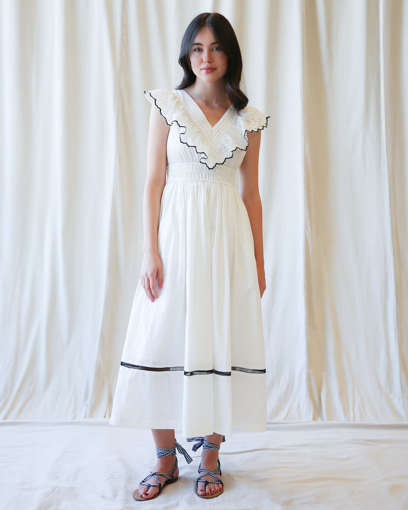 Woman wearing a white dress with black trim against a white curtain background