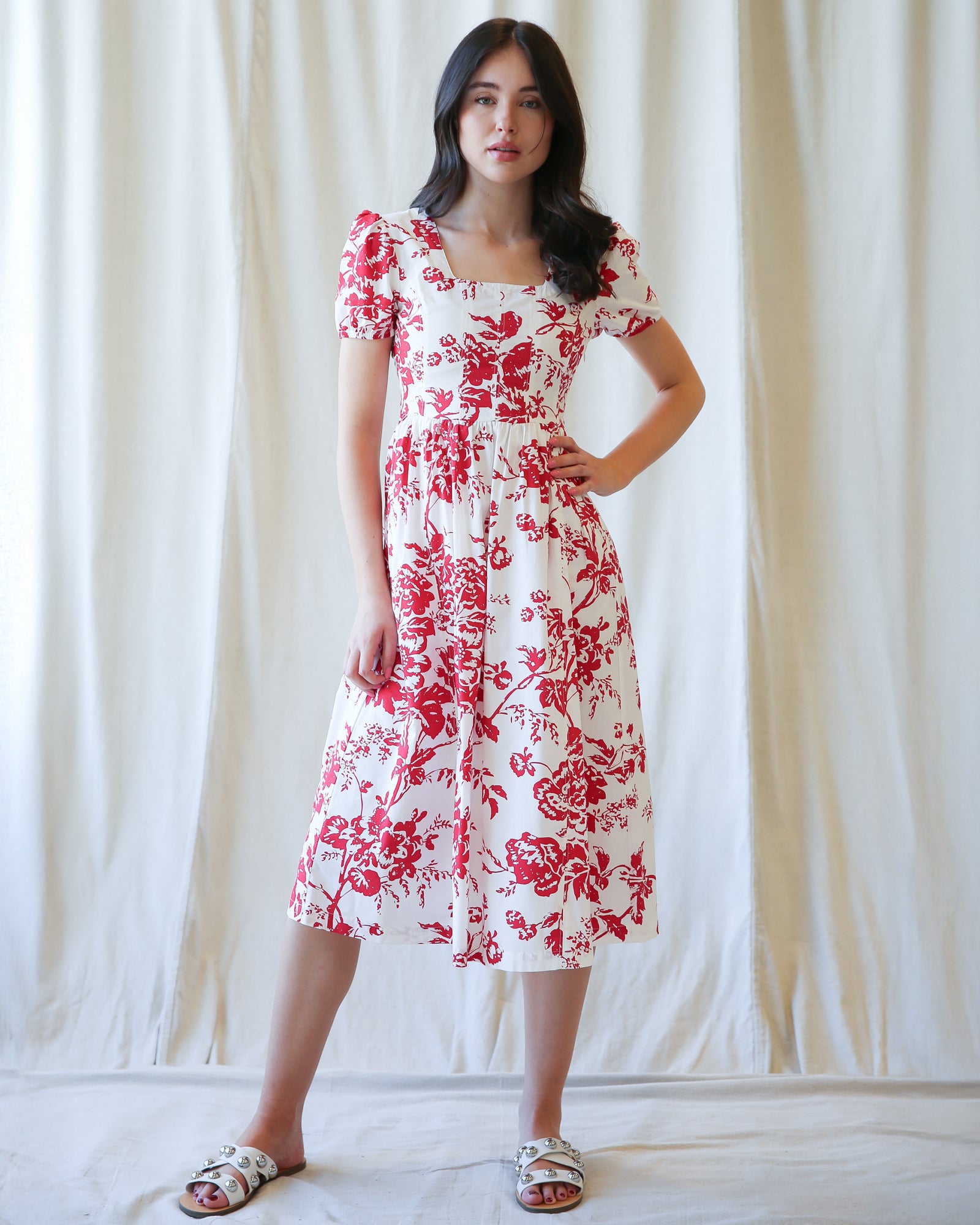 Woman wearing a white dress with red floral pattern against a plain background