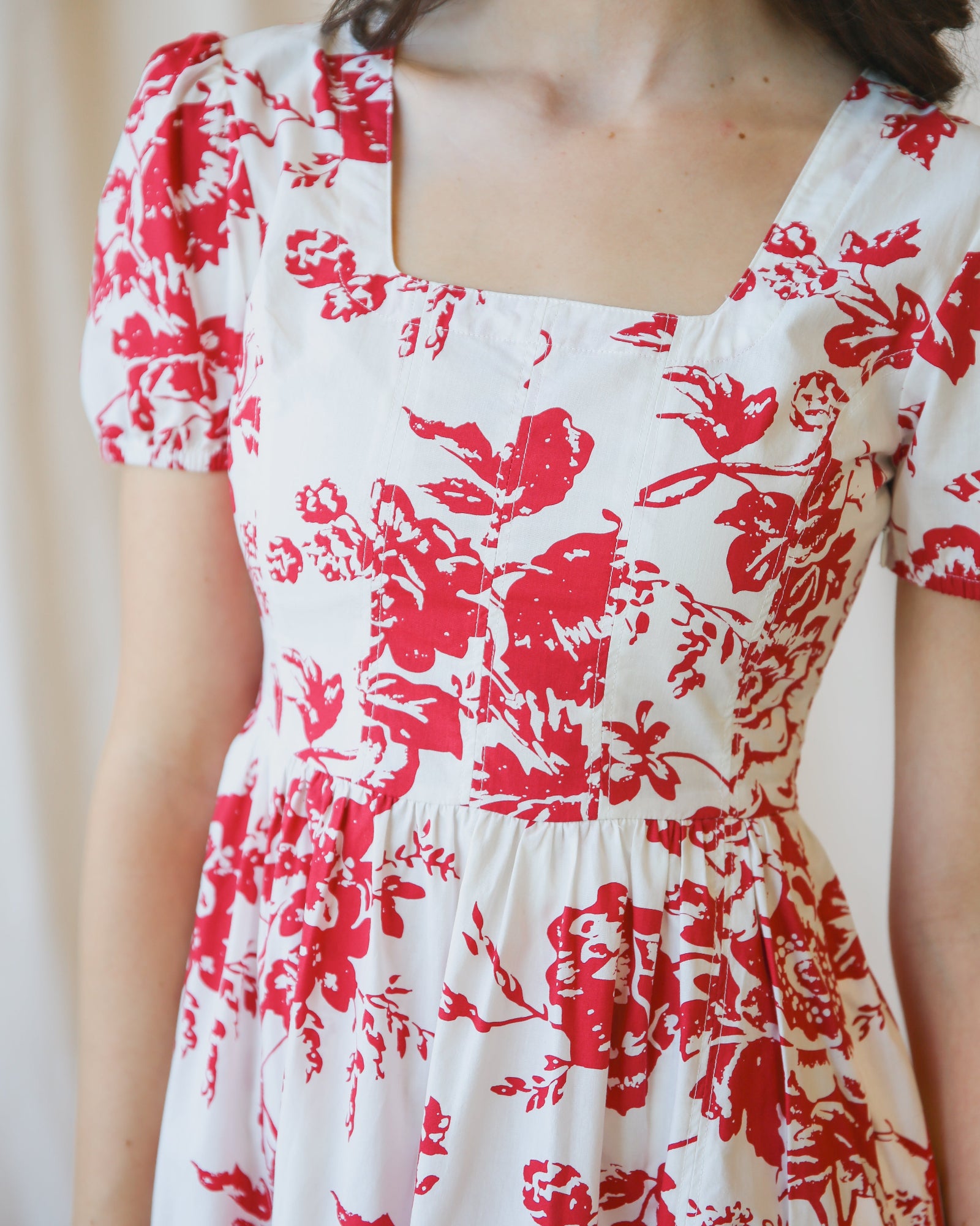 Close up Image of woman wearing a white dress with red floral print standing in front of a white canvas background