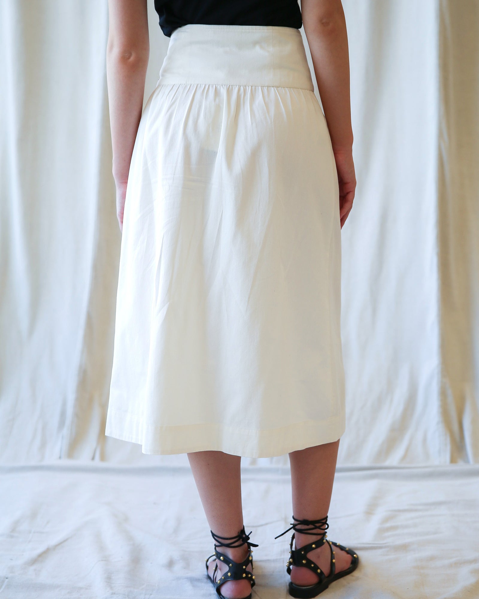 Person wearing a white skirt against a white curtain background