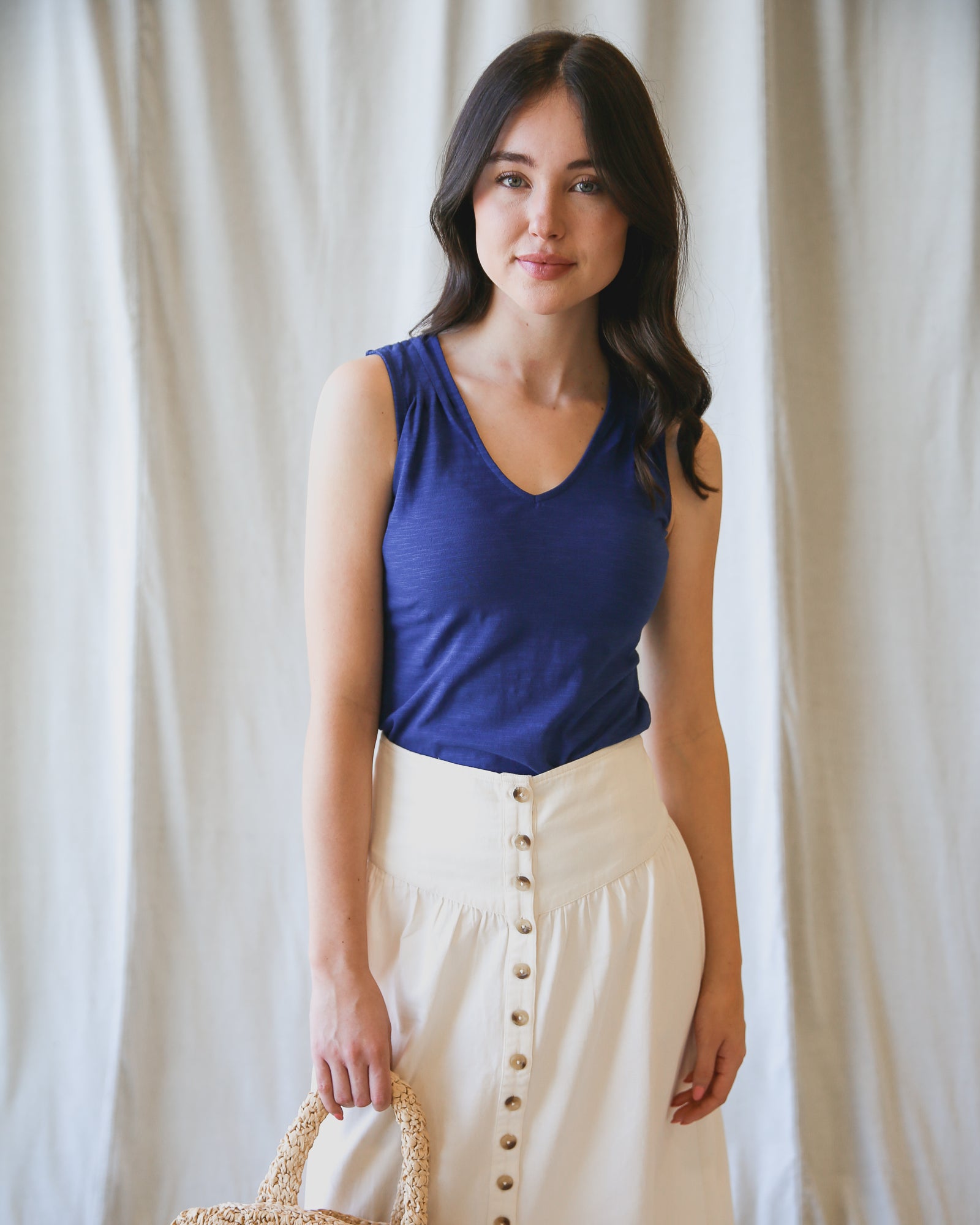 Woman wearing a blue tank top and white skirt with buttons against a plain background