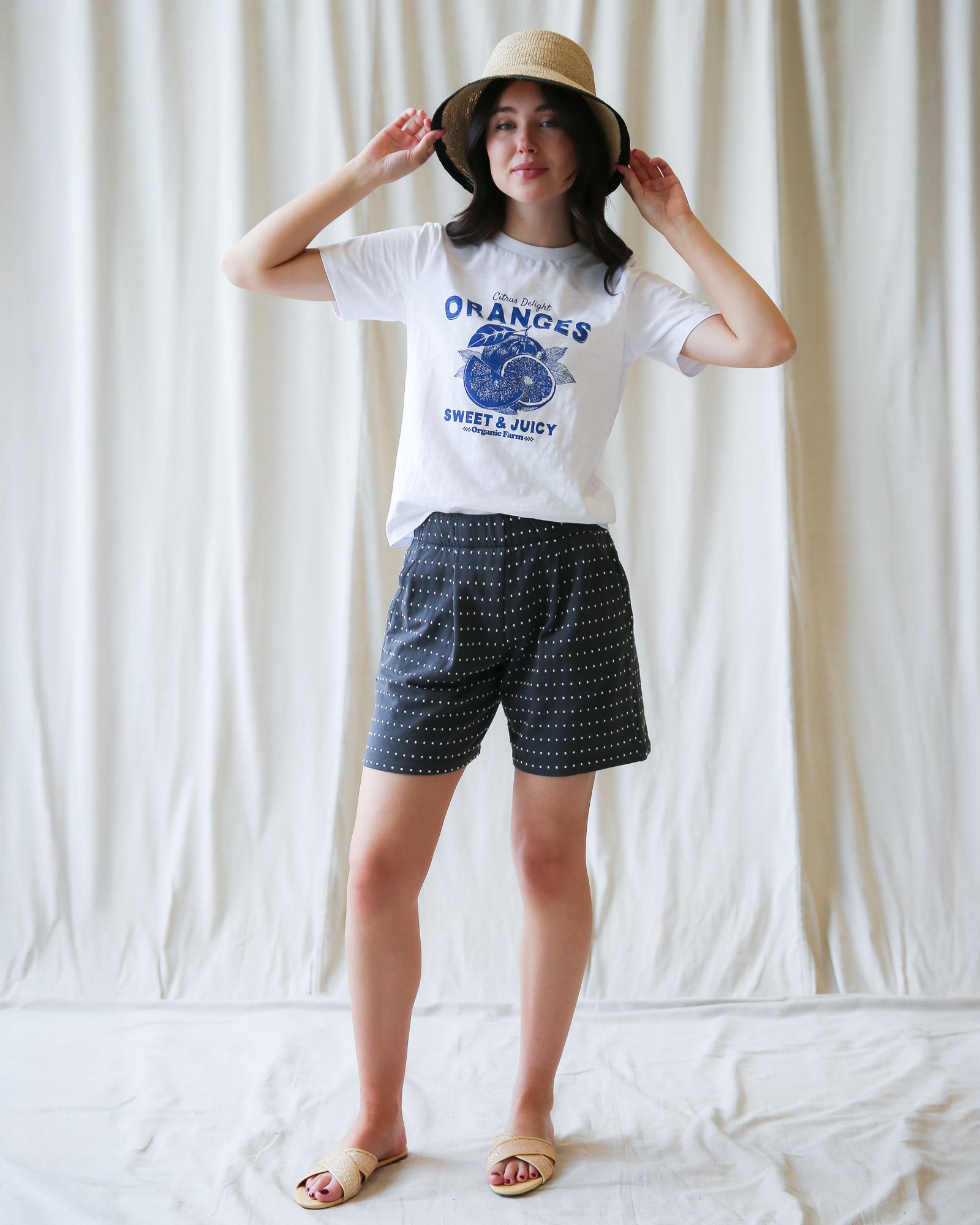 Person wearing a white t-shirt with a graphic design and black shorts against a plain background