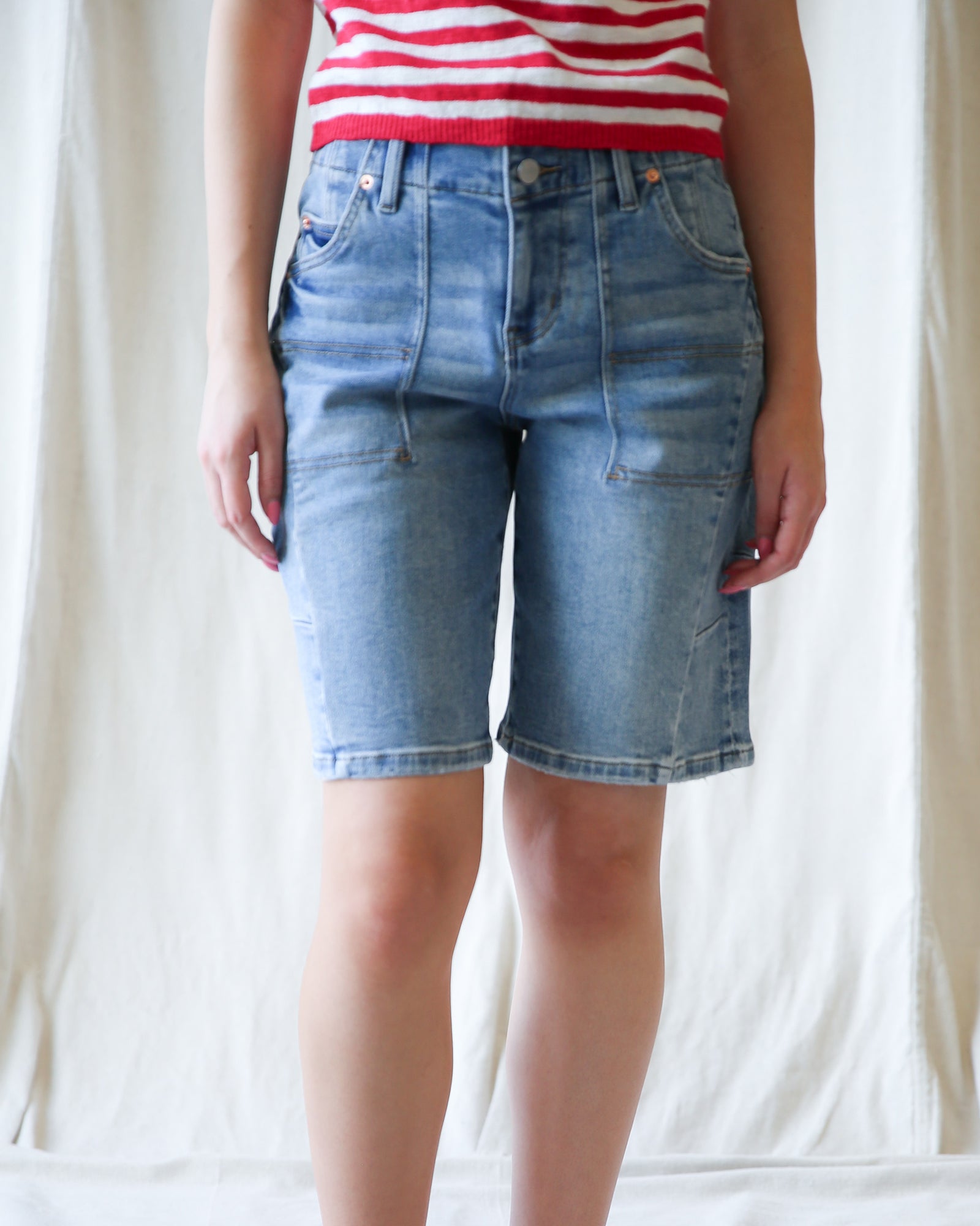 Person wearing blue denim shorts and a red and white striped shirt against a plain background