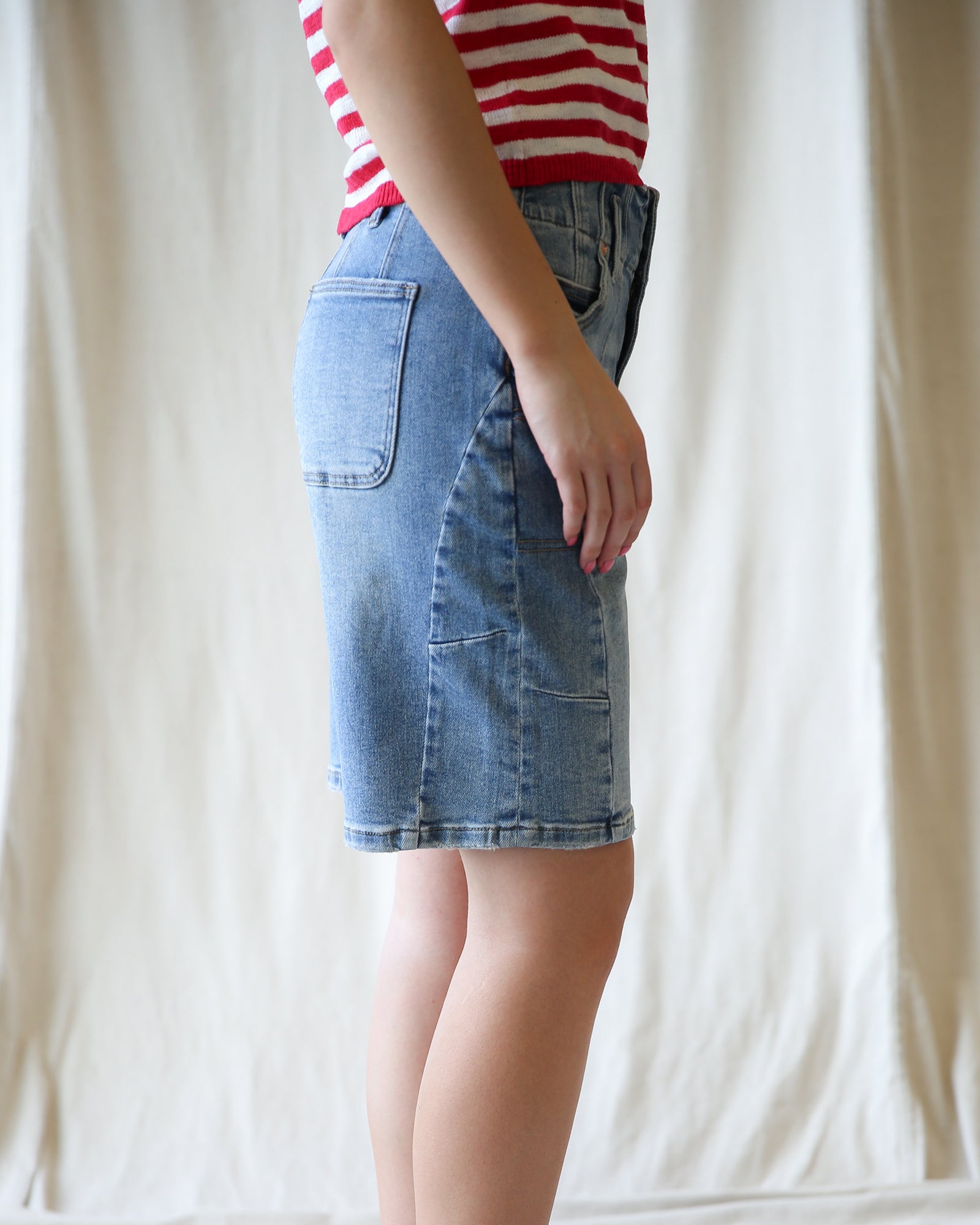 Person wearing a red and white striped shirt with a blue denim skirt against a plain background