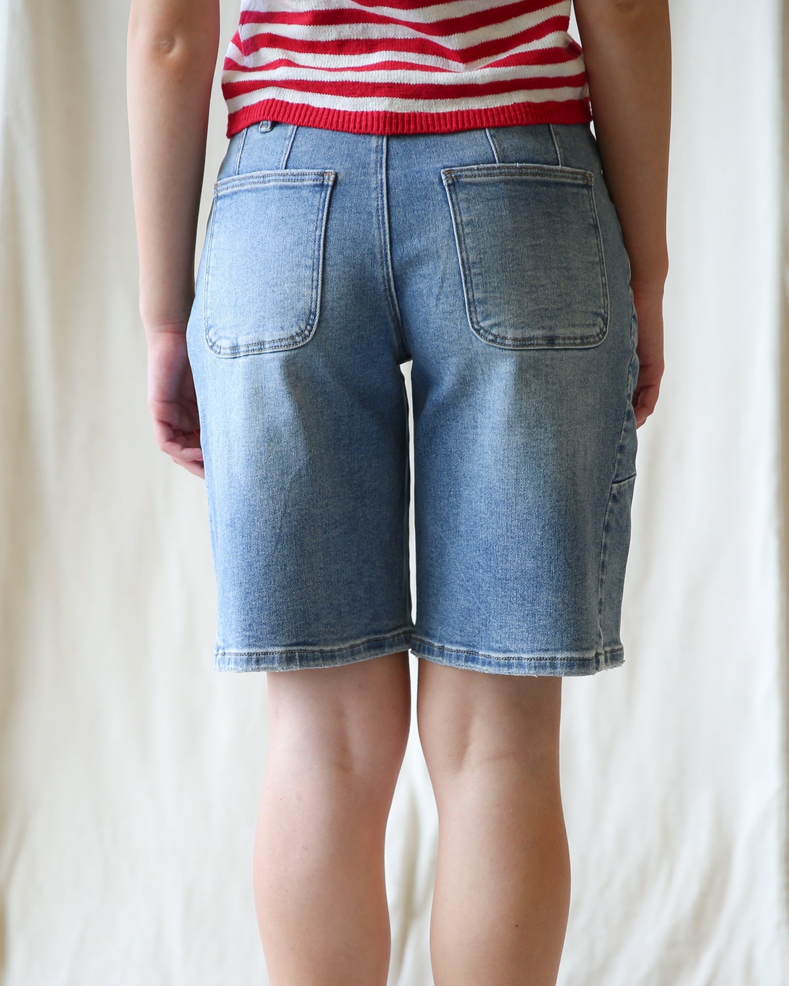 Person wearing blue denim shorts and a red and white striped shirt on a plain background