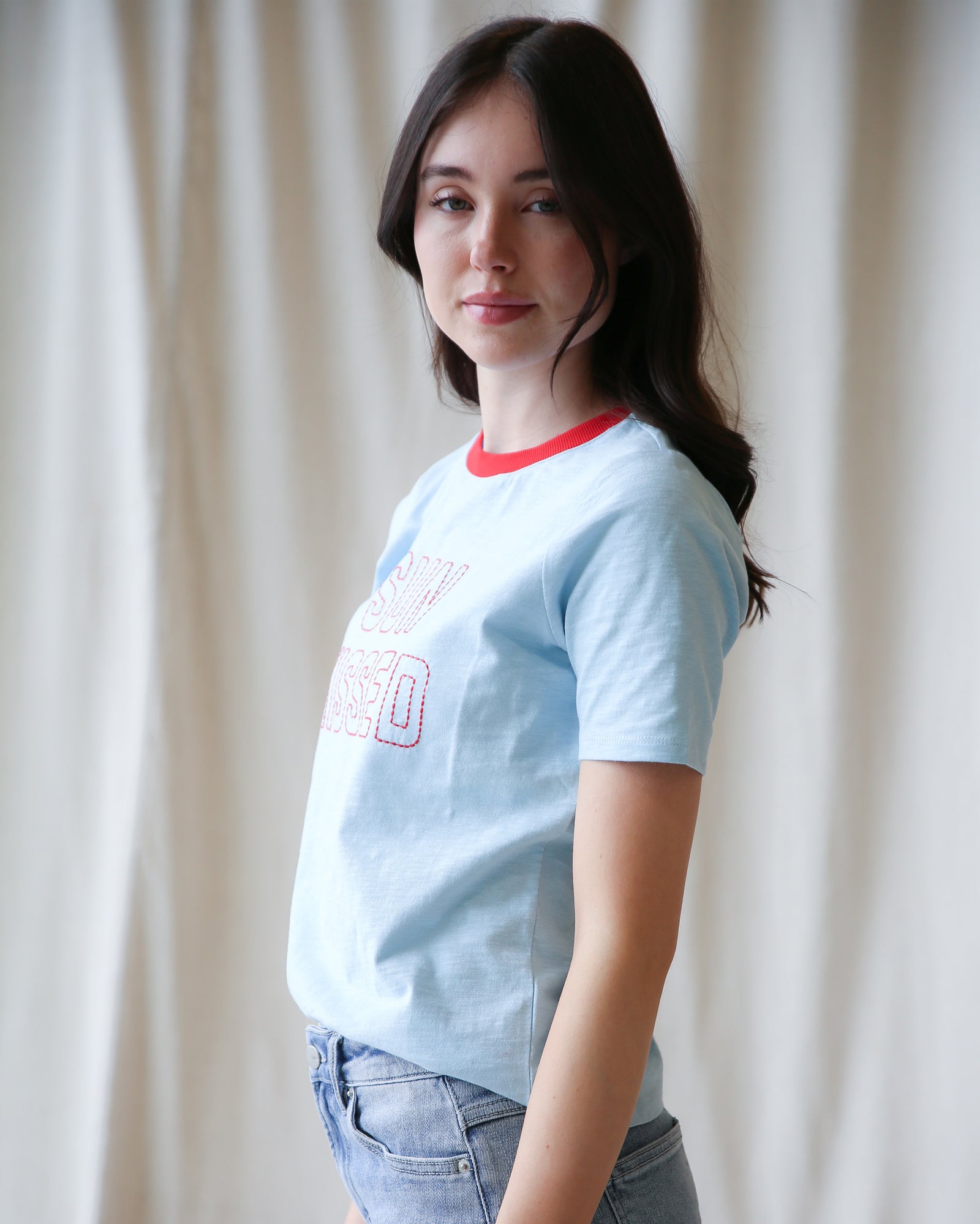 Woman wearing a light blue t-shirt with red text against a white curtain background