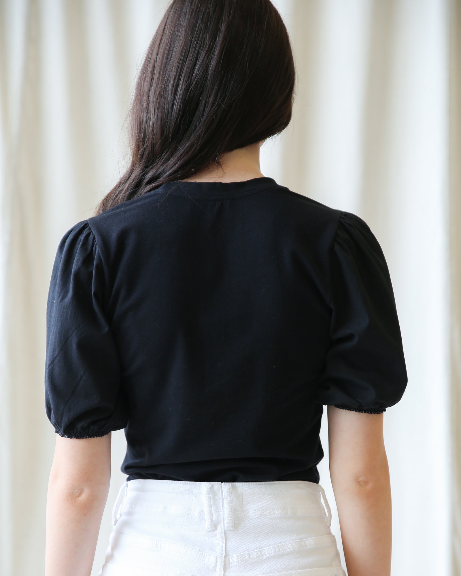 Person wearing a black top with puff sleeves against a white curtain background