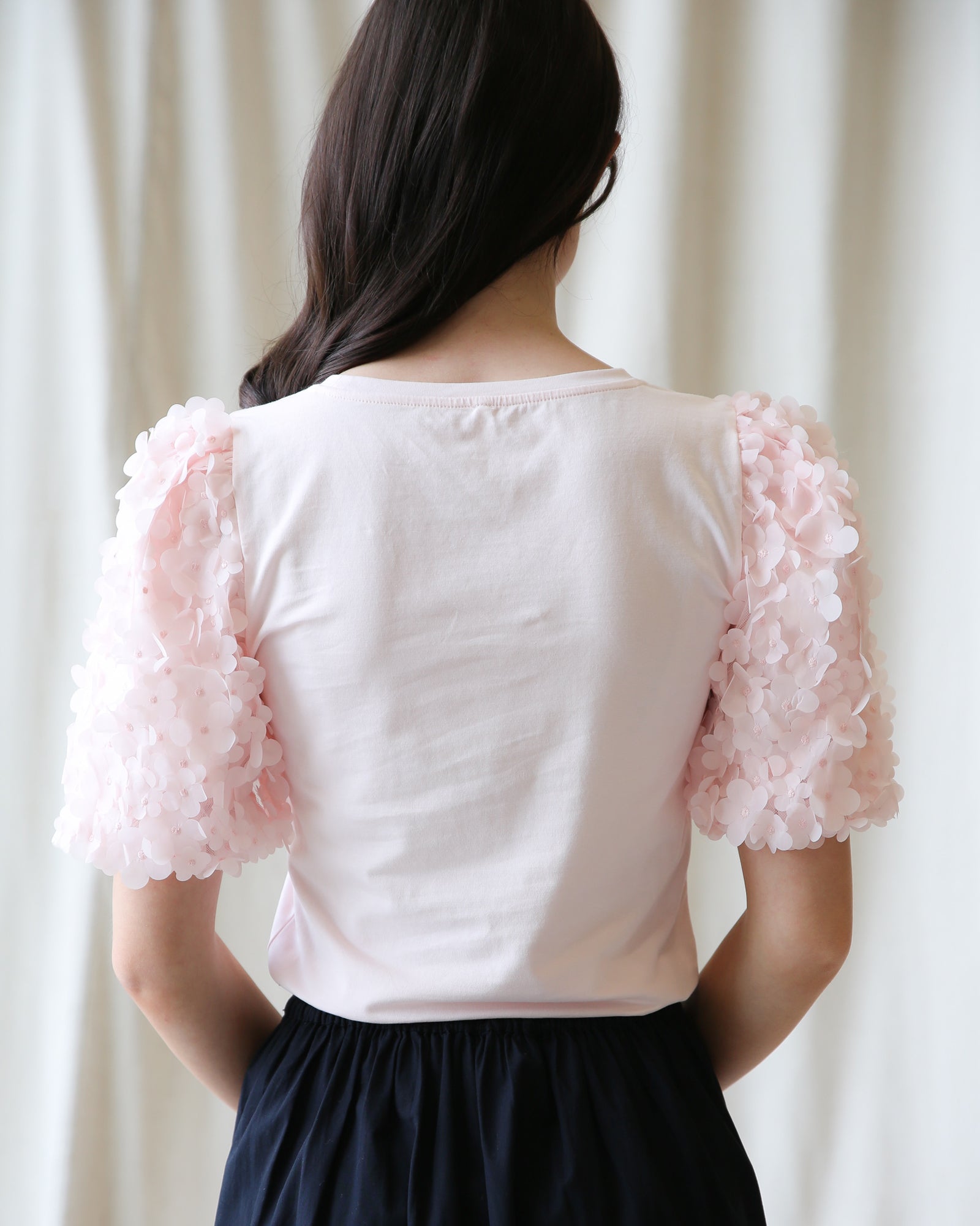 Woman wearing a white blouse with pink floral sleeves against a white curtain background