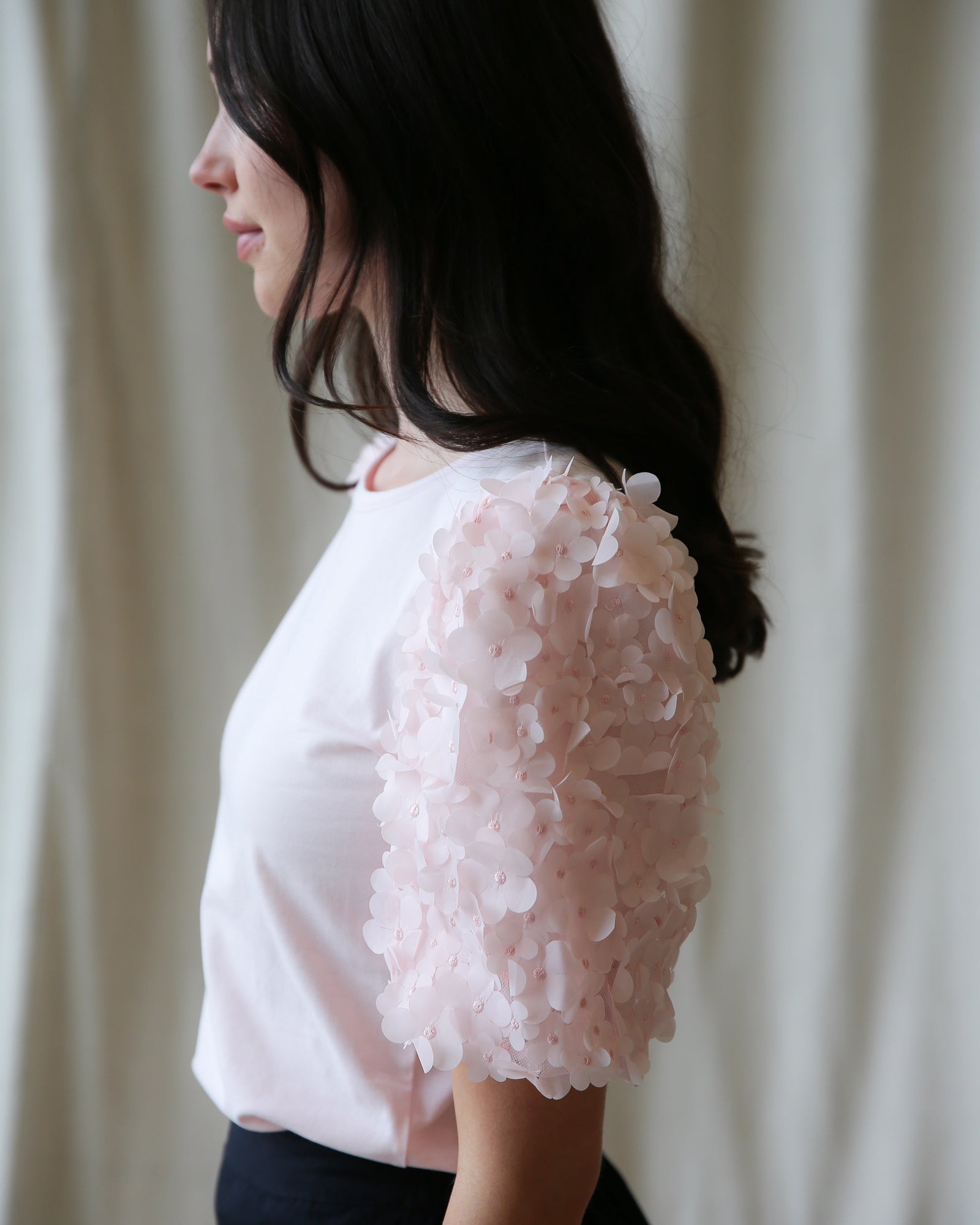 Woman wearing a light pink blouse with floral details against a neutral background