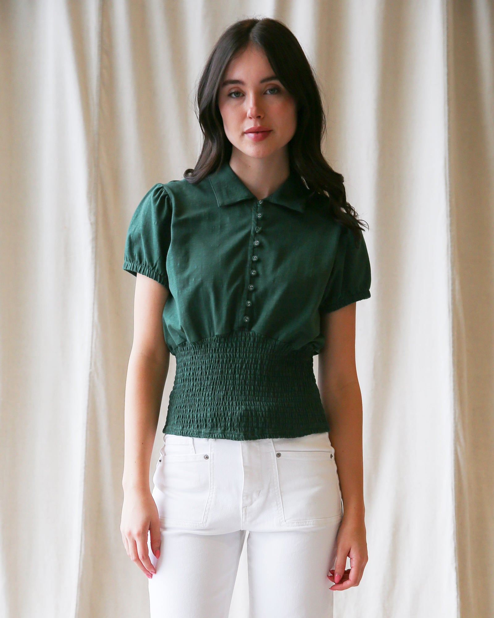 Woman wearing a green blouse with puff sleeves against a beige curtain background