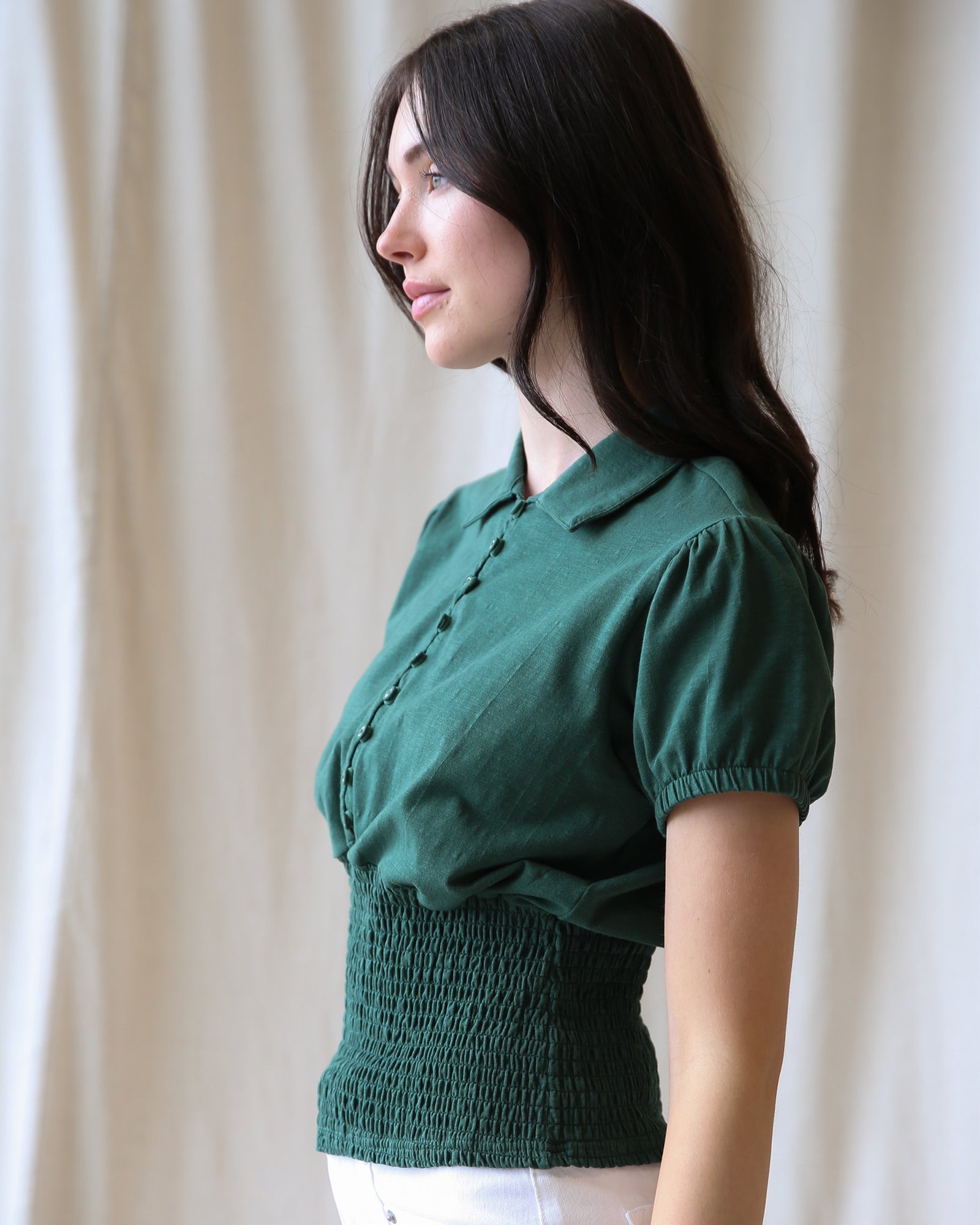 Woman wearing a green blouse against a beige curtain background