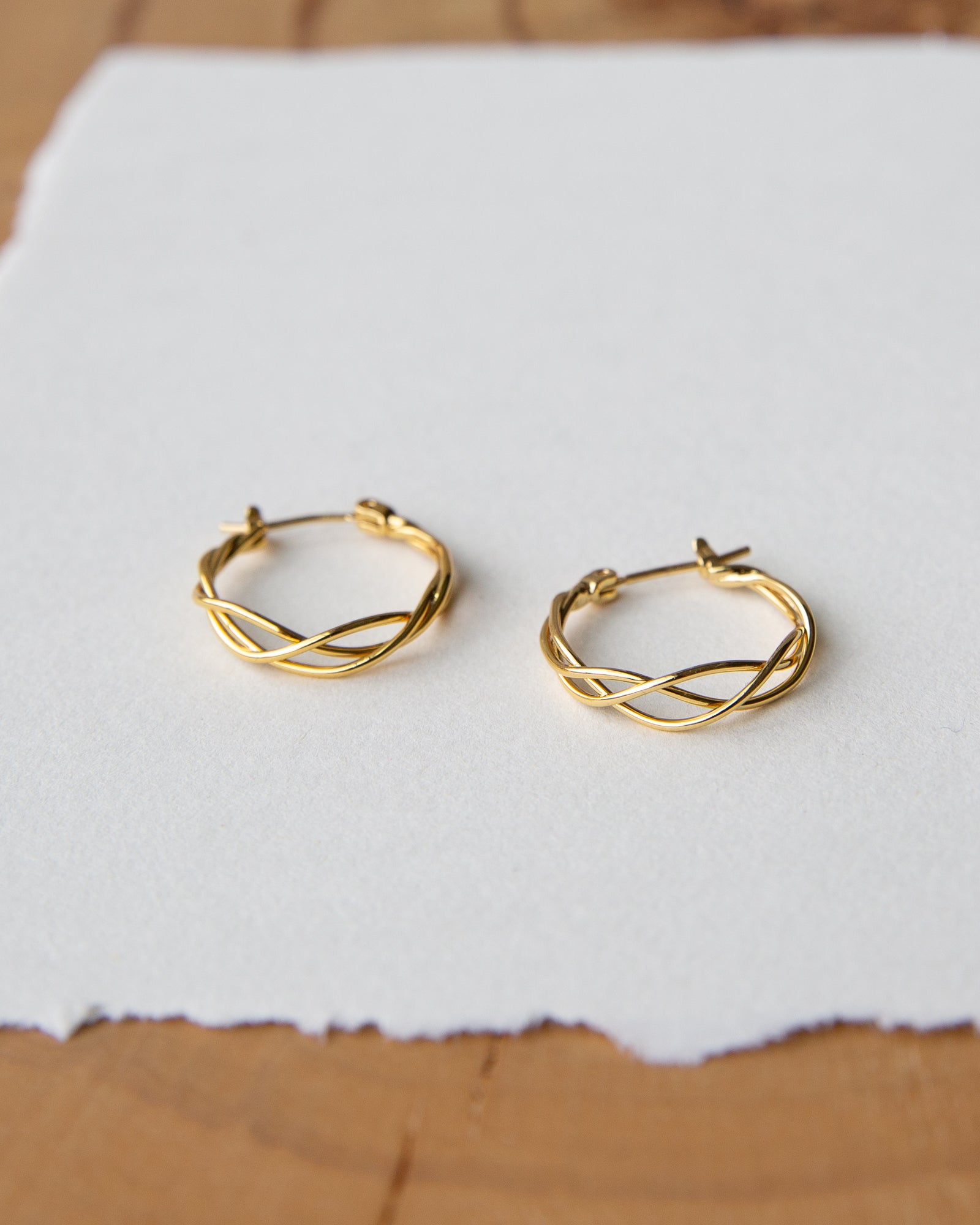 Gold hoop earrings on a white paper background