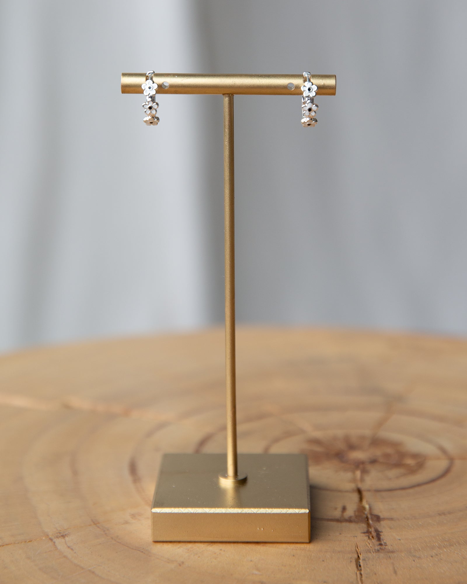 Gold earring stand with earrings on a wooden surface and gray background
