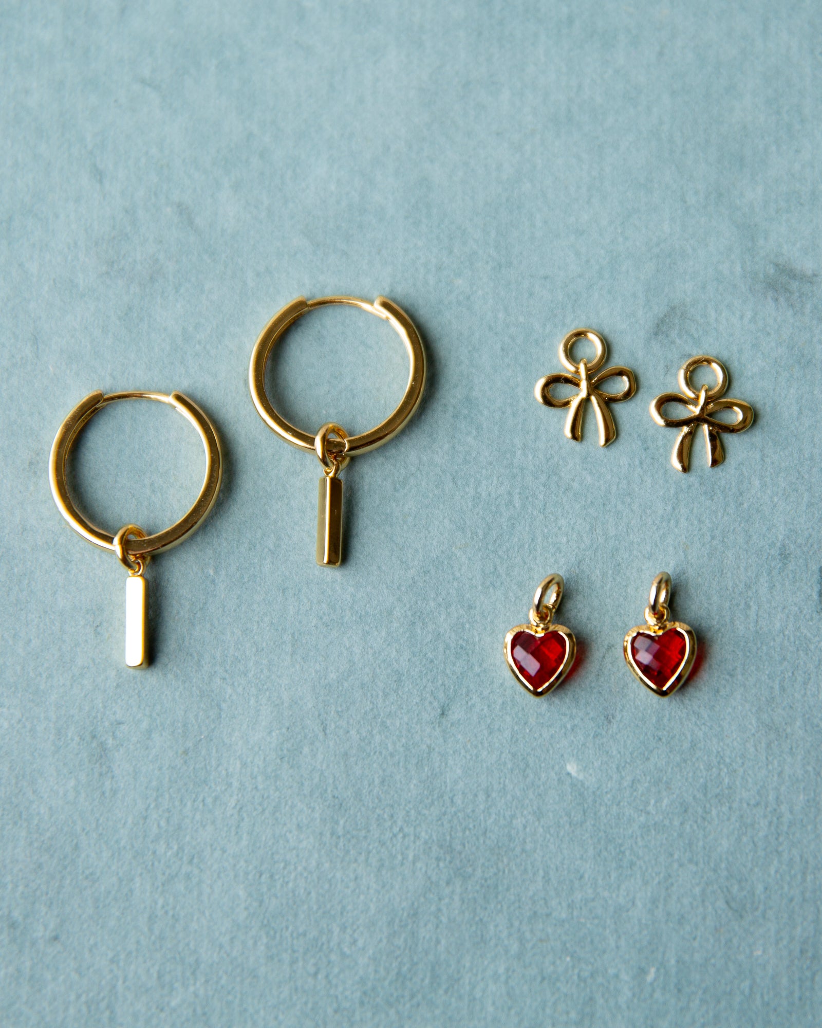 Gold hoop earrings and red heart pendants on a light blue background