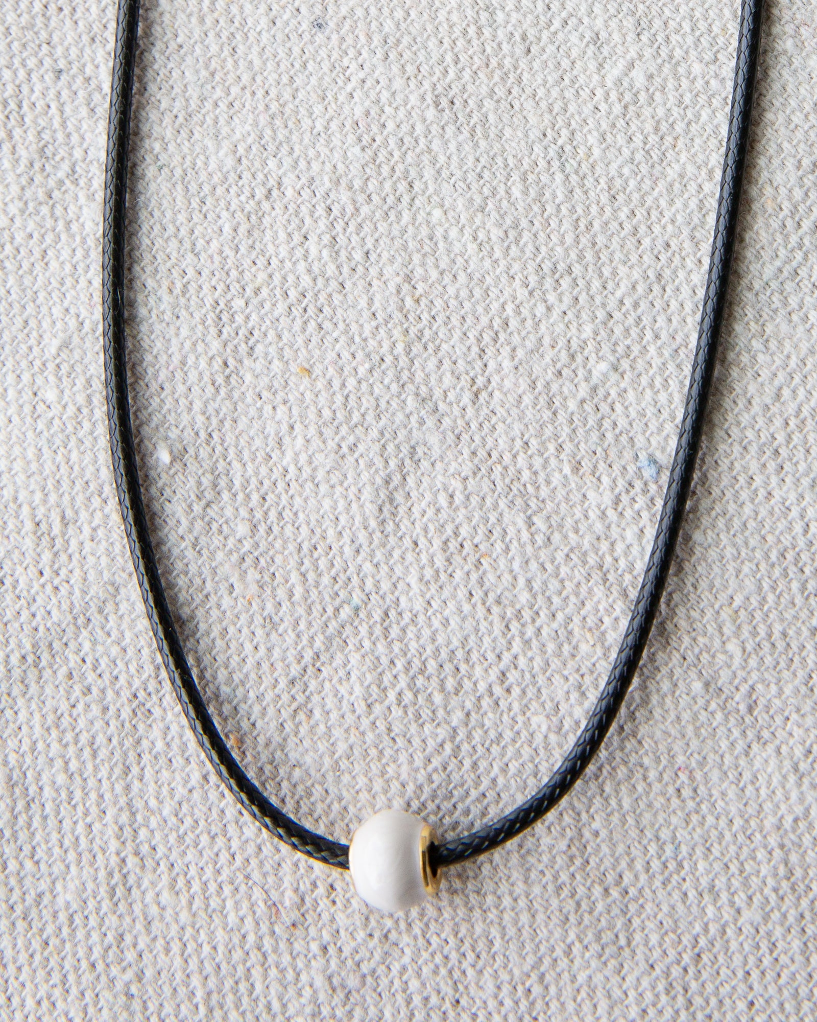 Necklace with a white bead on a textured beige background