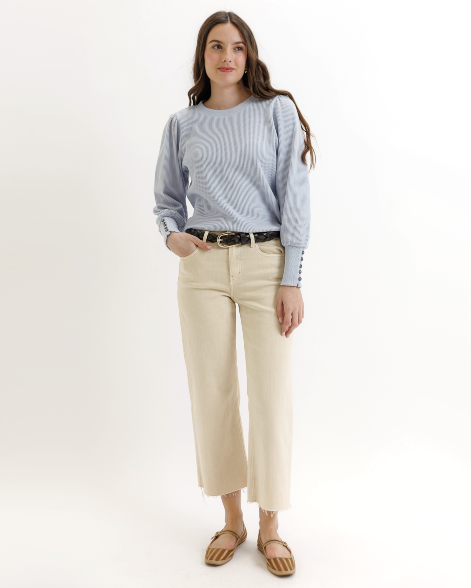 Woman wearing a light blue textured top and beige pants on a white background
