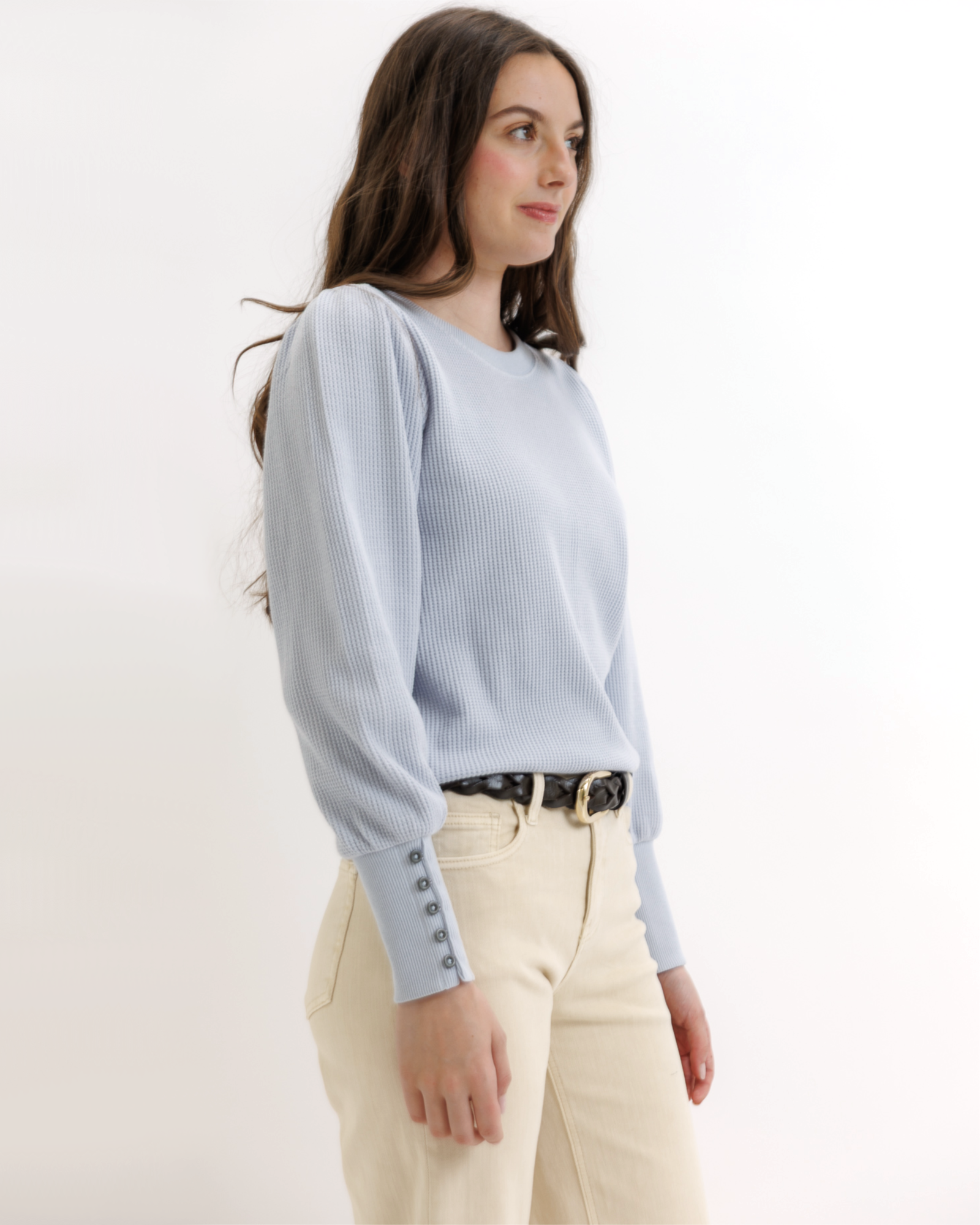 Woman wearing a light blue textured top and beige pants on a white background