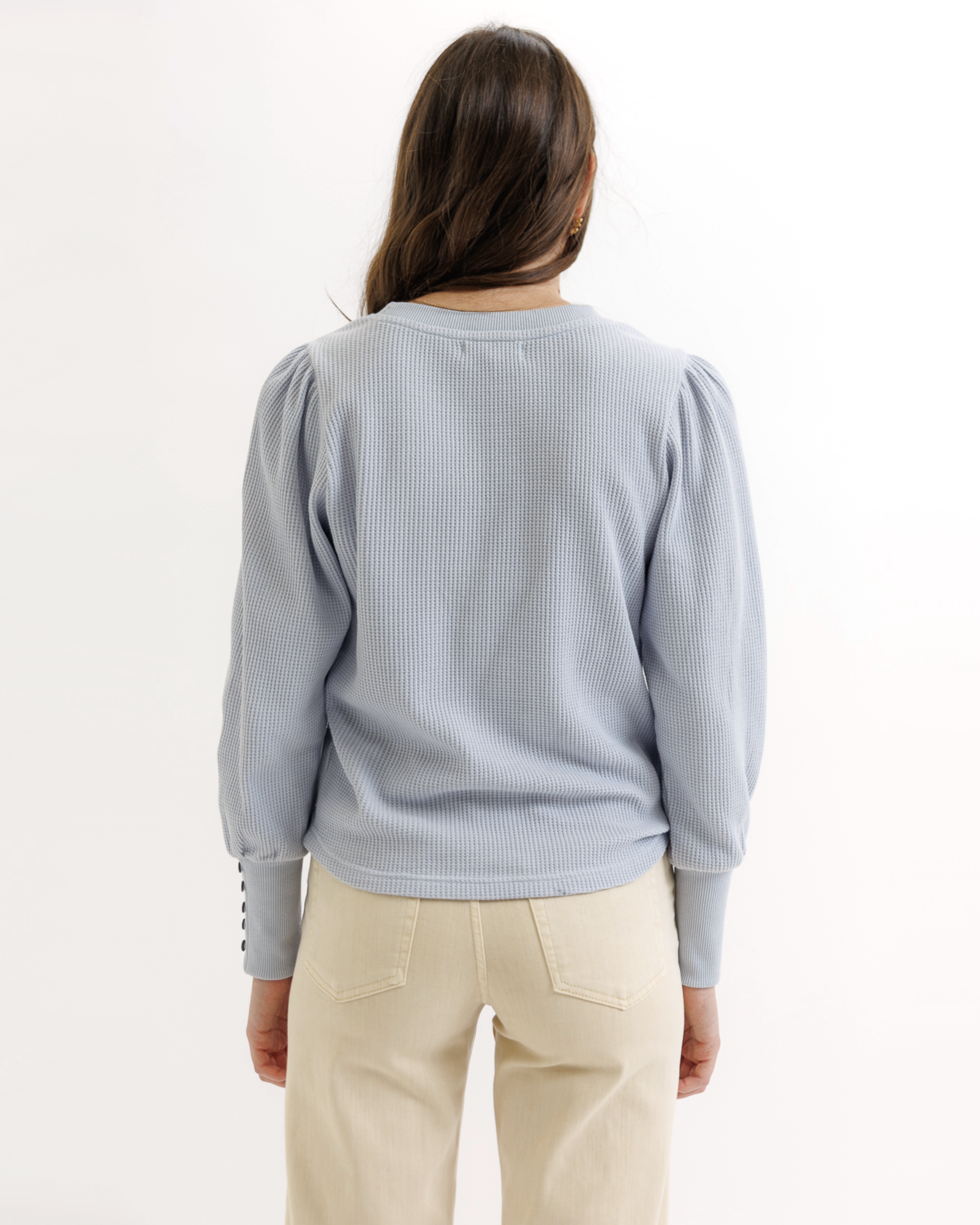 Woman wearing a light blue textured top and beige pants on a white background
