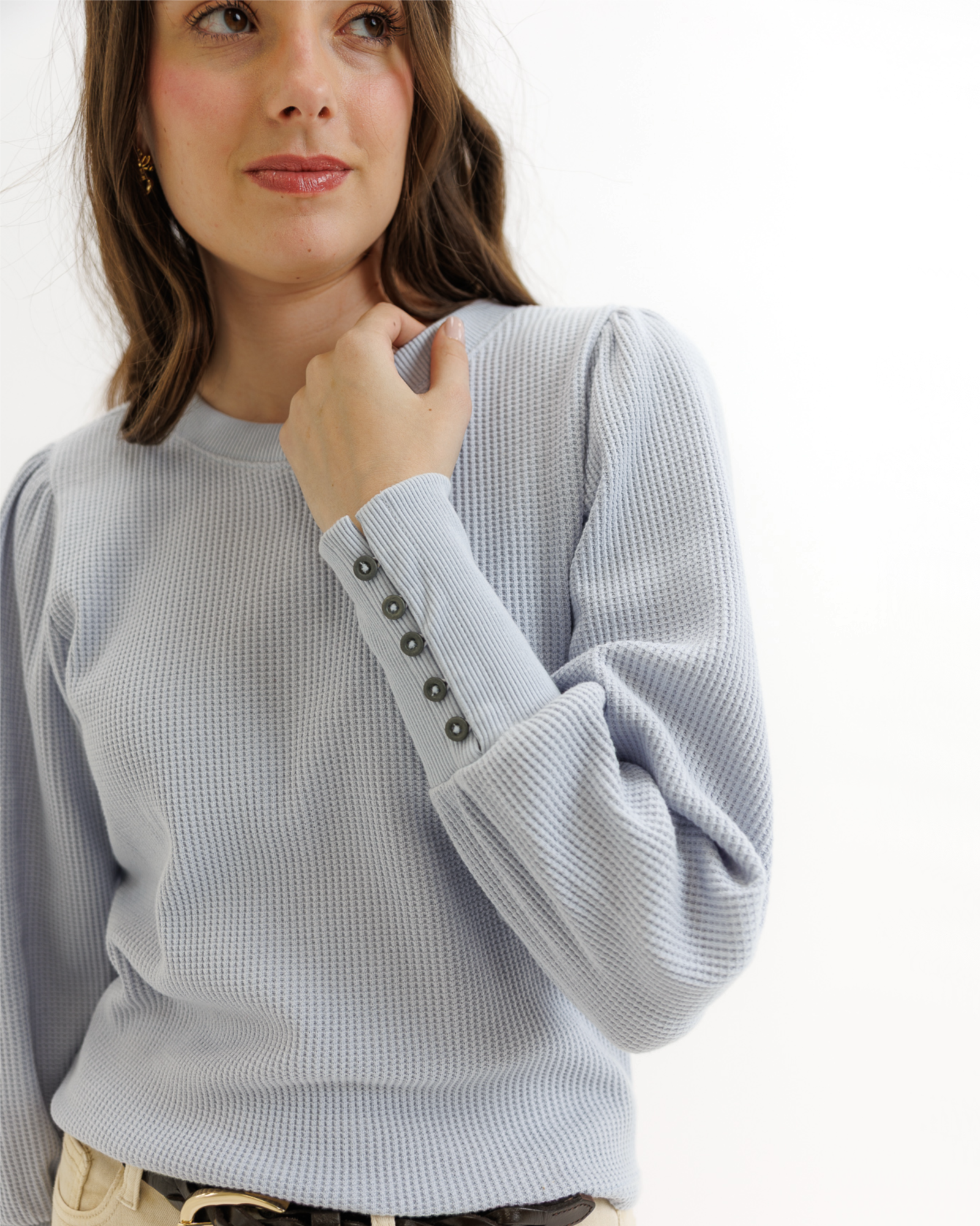 Woman wearing a light blue textured top and beige pants on a white background