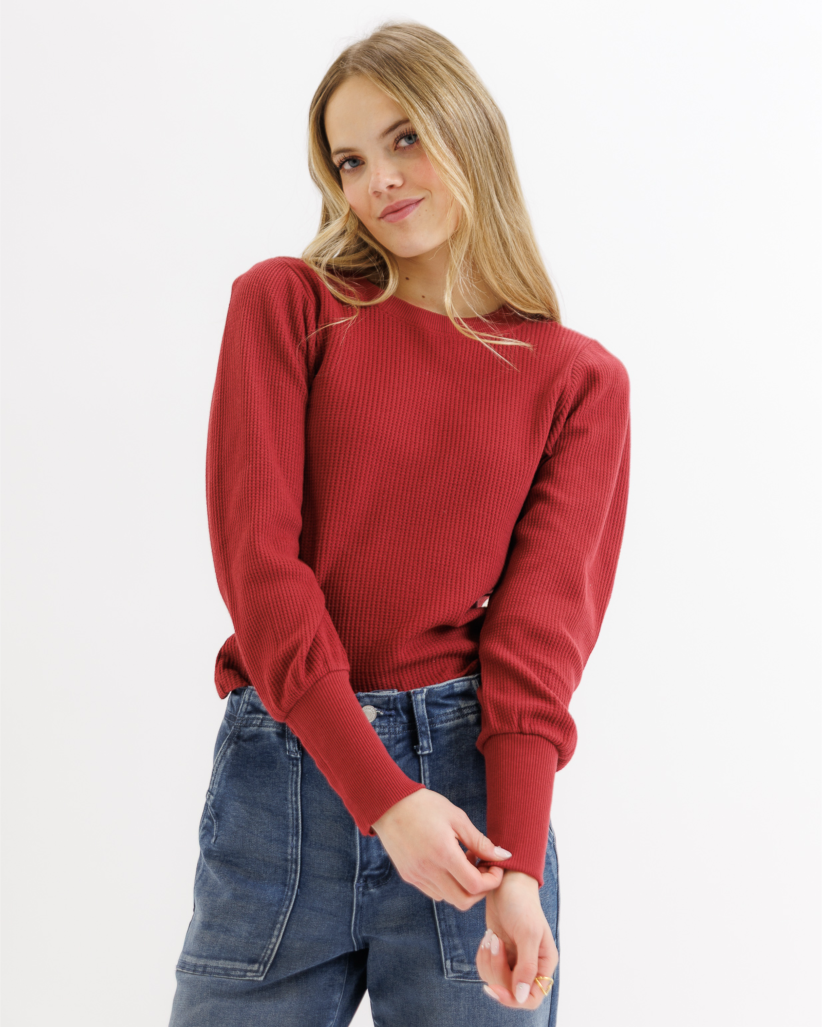Woman wearing a red textured top and blue jeans on a white background