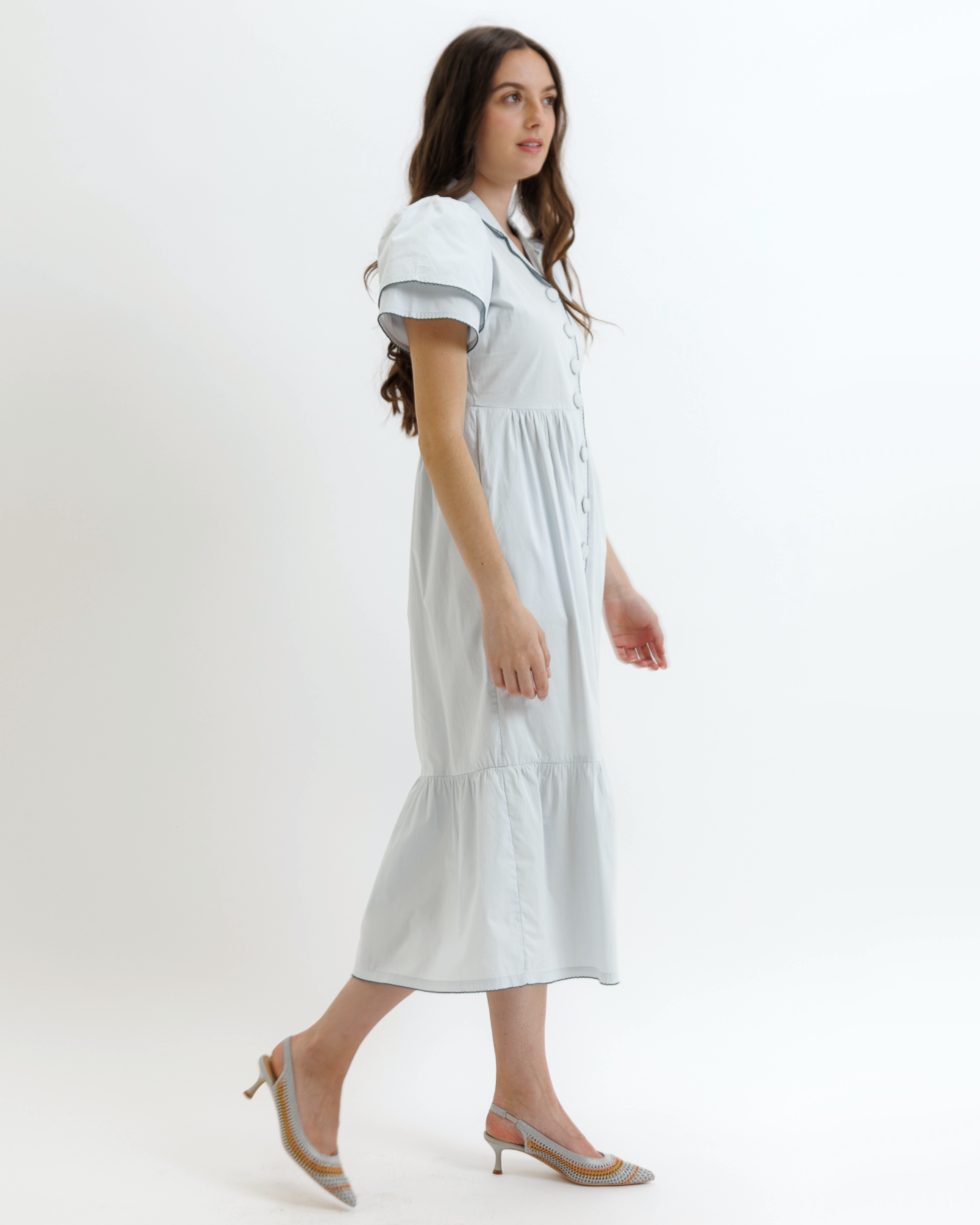 Woman wearing a light blue dress with buttons on a white background