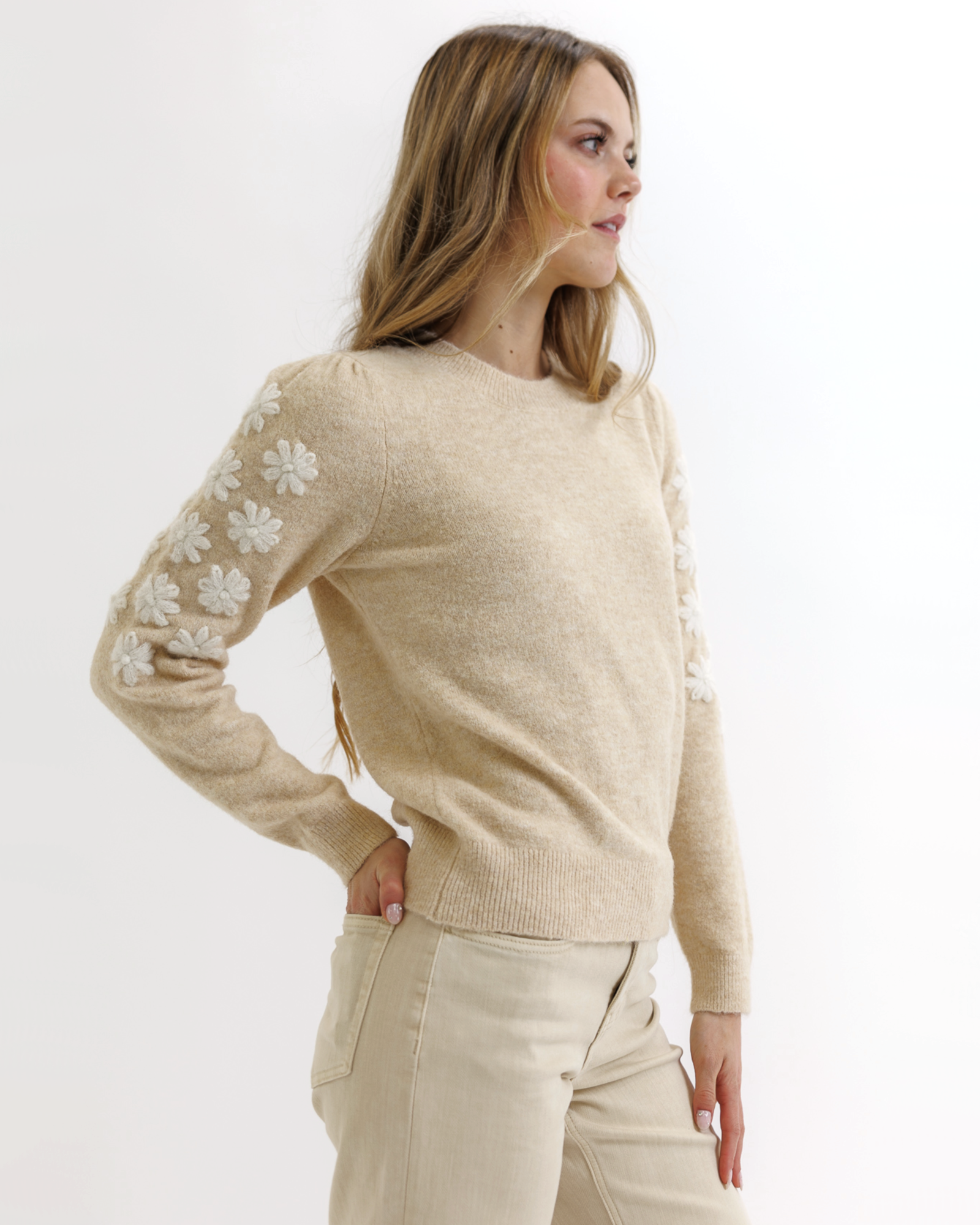 Woman wearing a beige sweater with white floral patterns on a white background