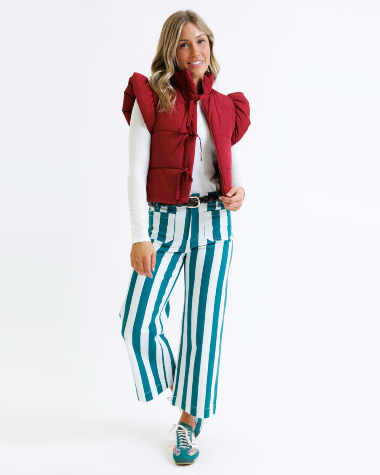 Woman wearing a red puffer vest and green striped pants on a white background
