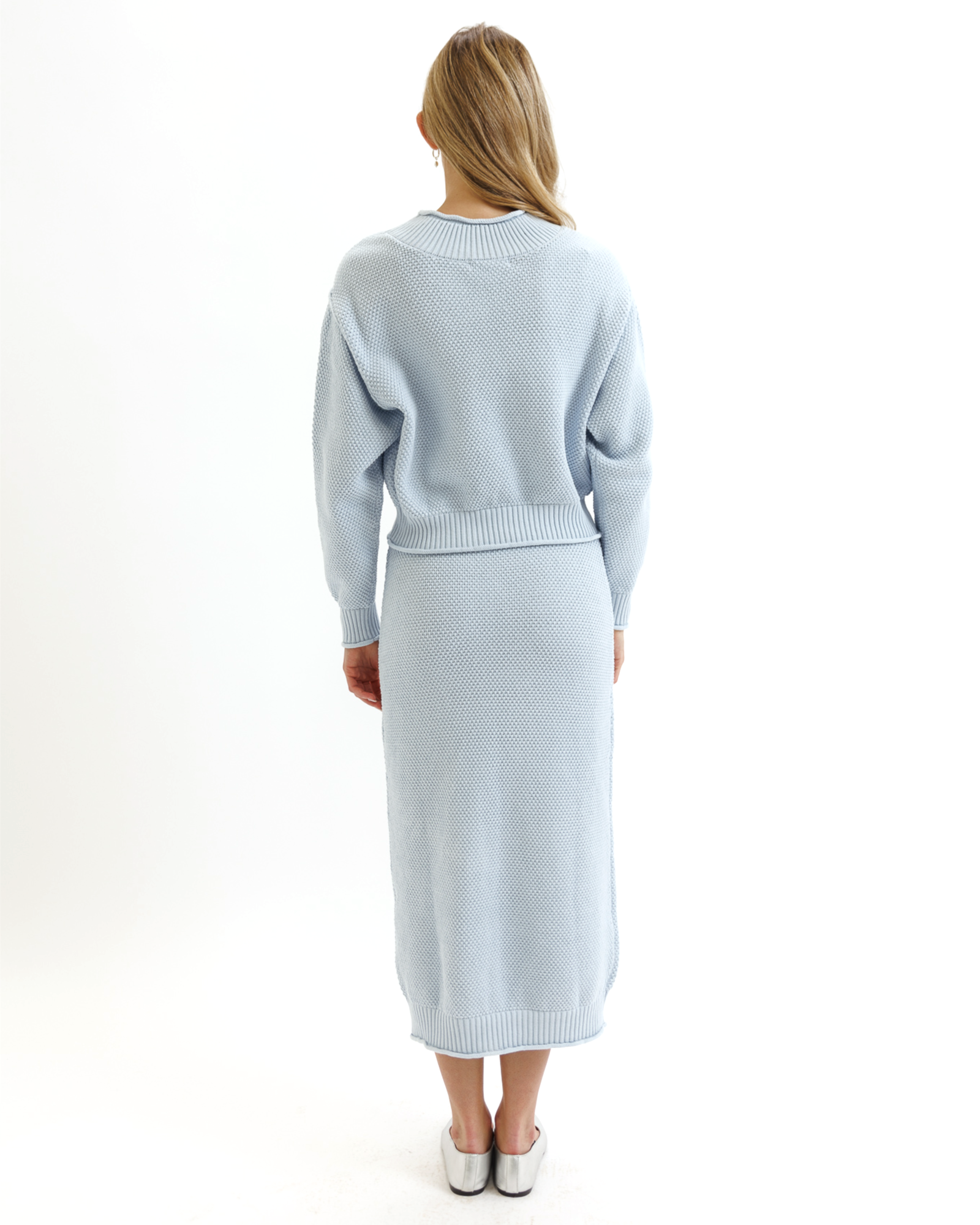 Woman wearing a light blue knitted sweater and skirt set on a white background