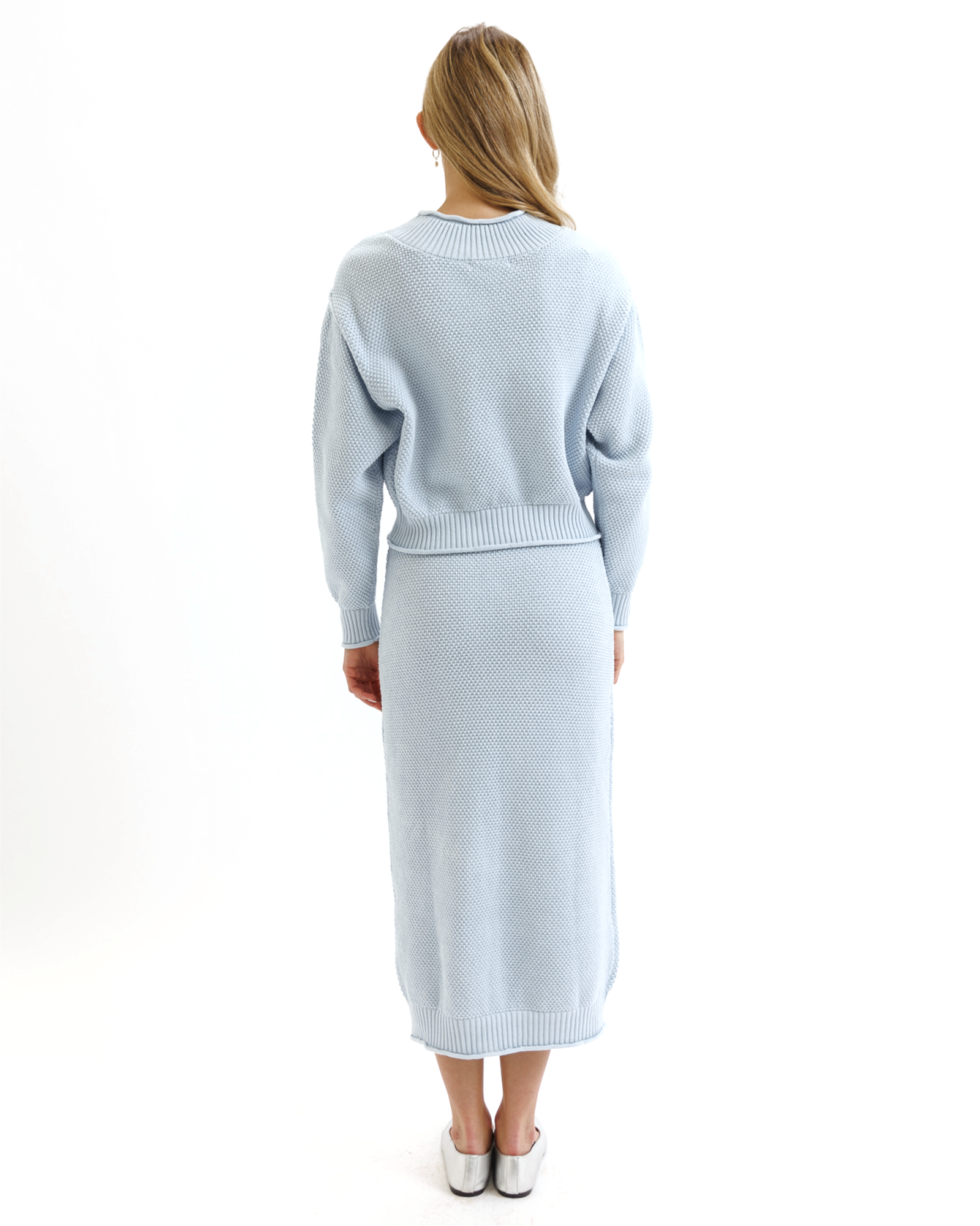 Woman wearing a light blue knitted sweater and skirt set on a white background