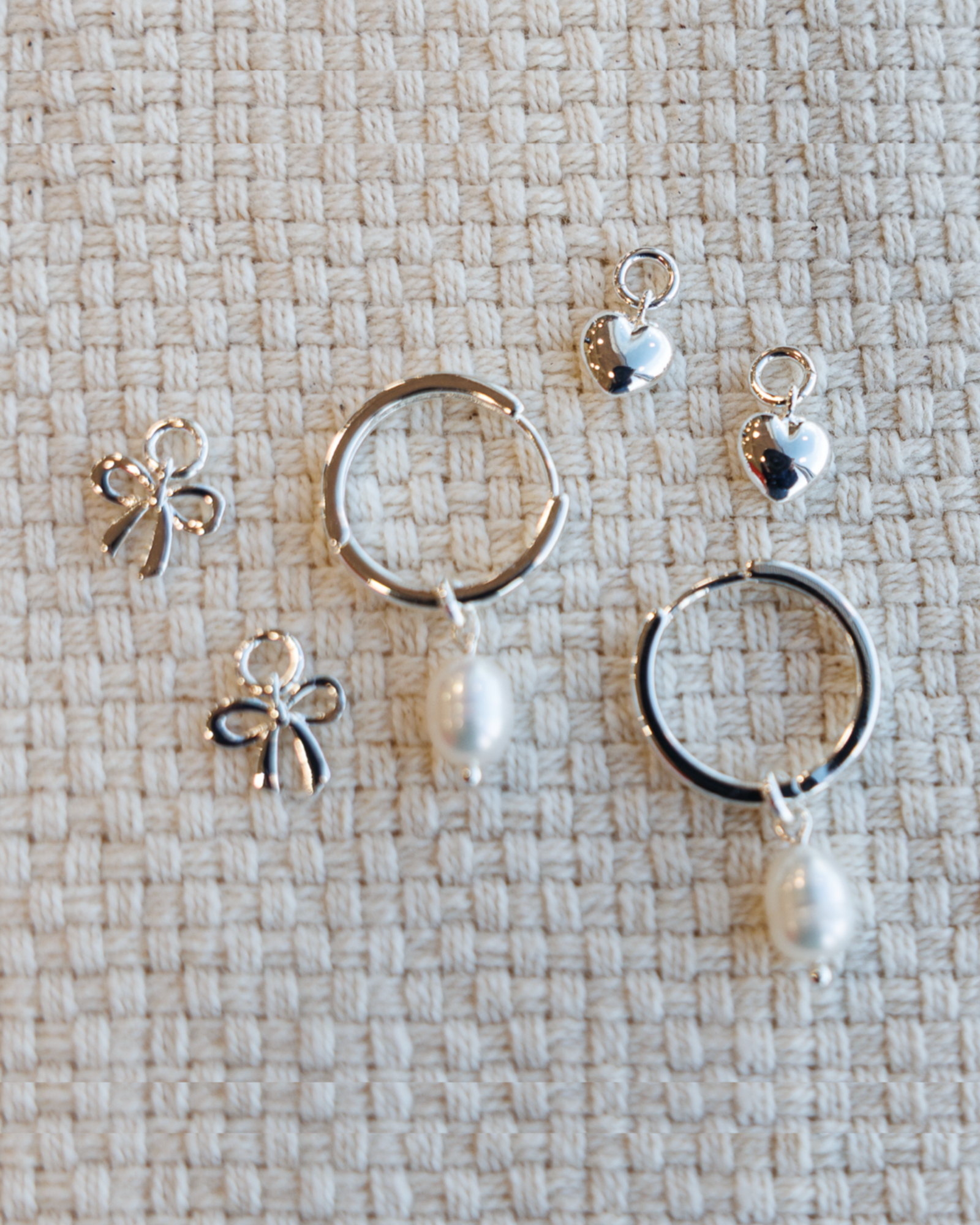Set of silver hoop earrings with miscellaneous charms on a textured beige surface