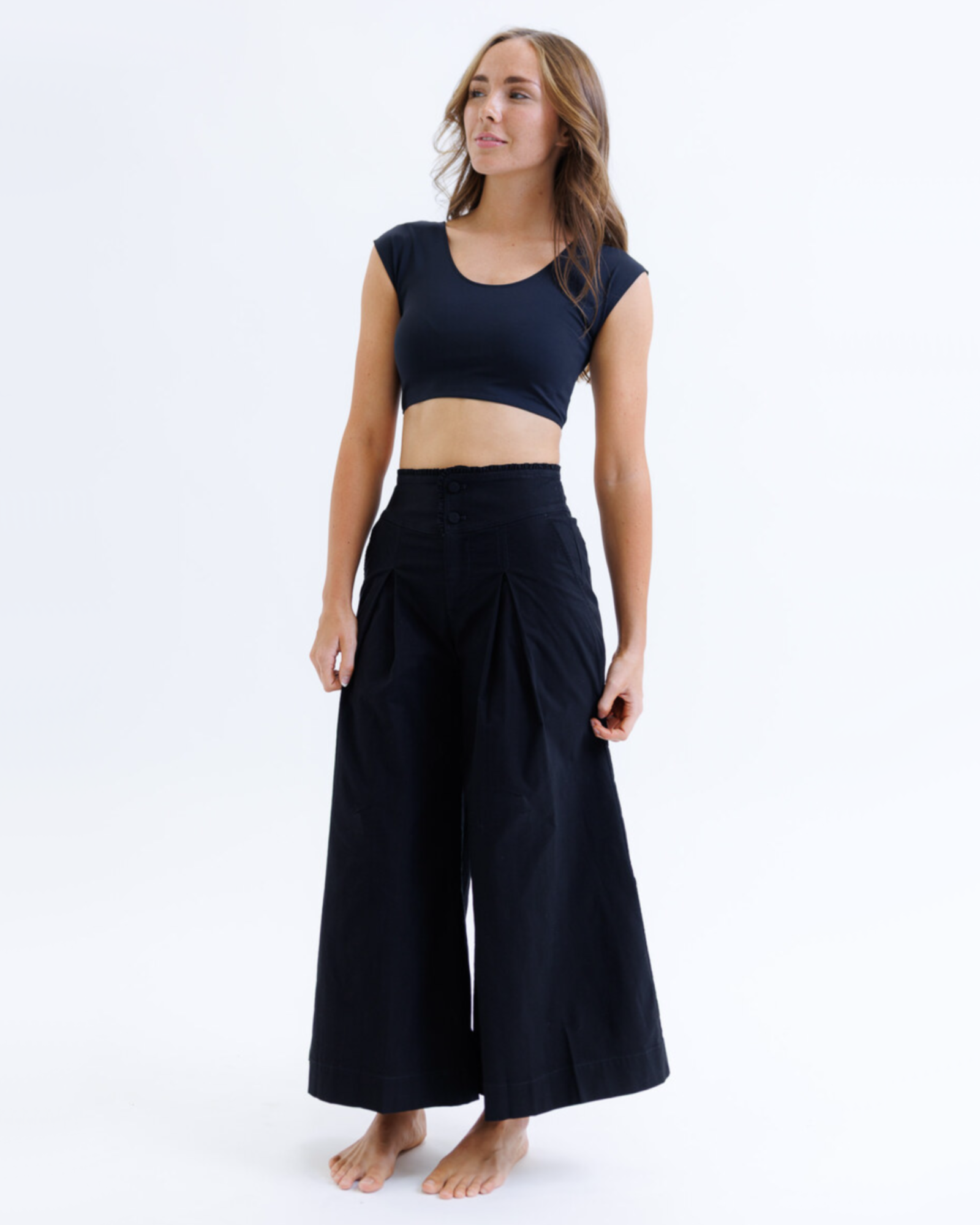 Woman wearing a black cropped layering top and black wide-leg pants on a white background