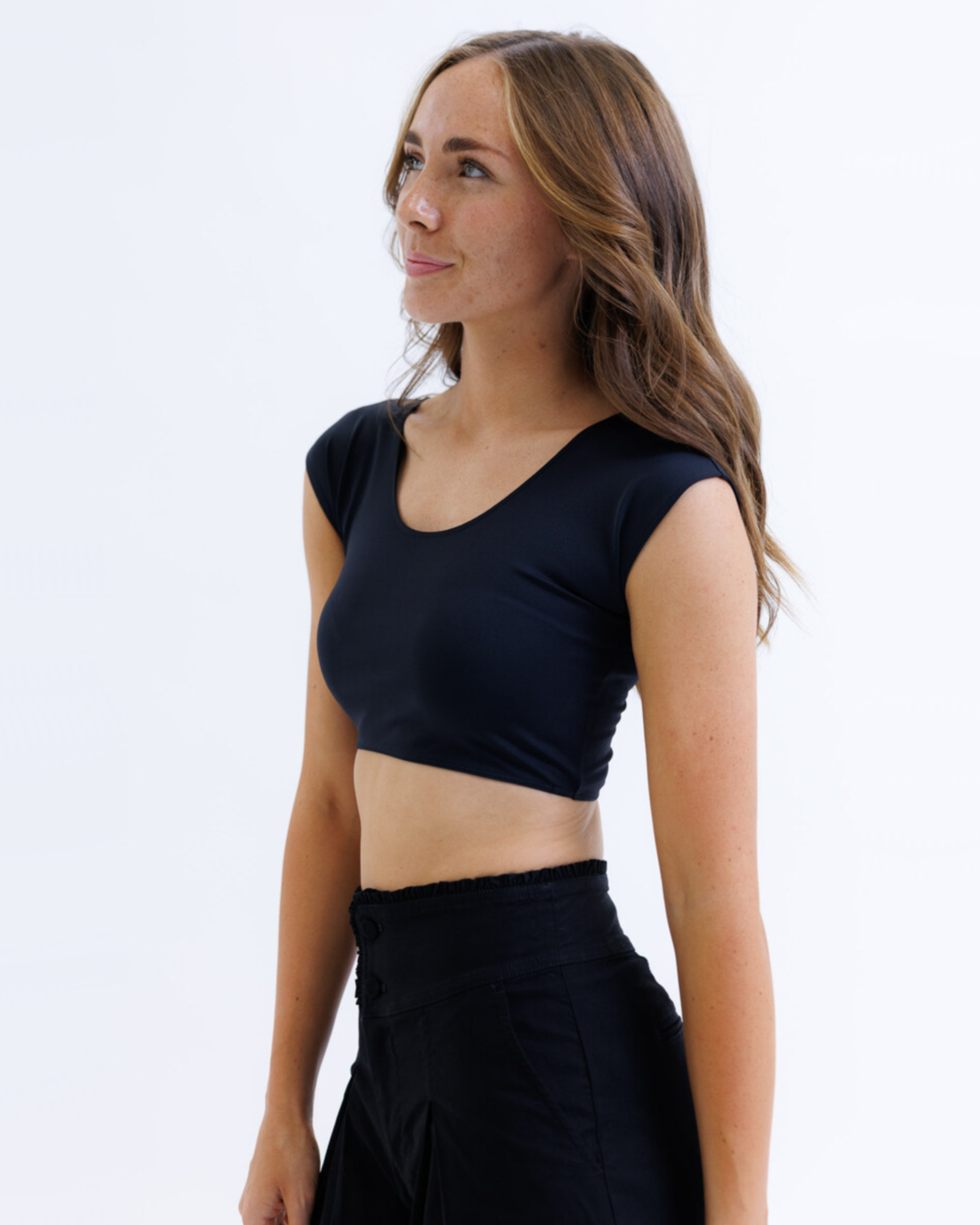 Woman wearing a black cropped layering top and black pants on a white background
