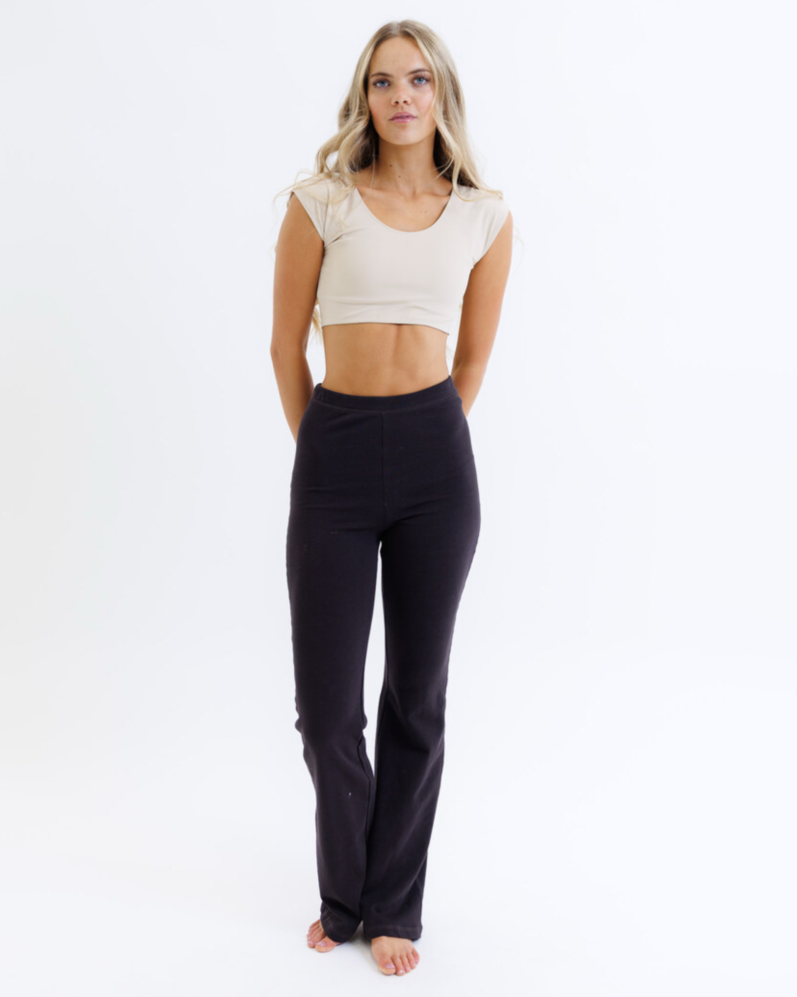 Woman wearing a nude cropped layering top and black pants on a white background