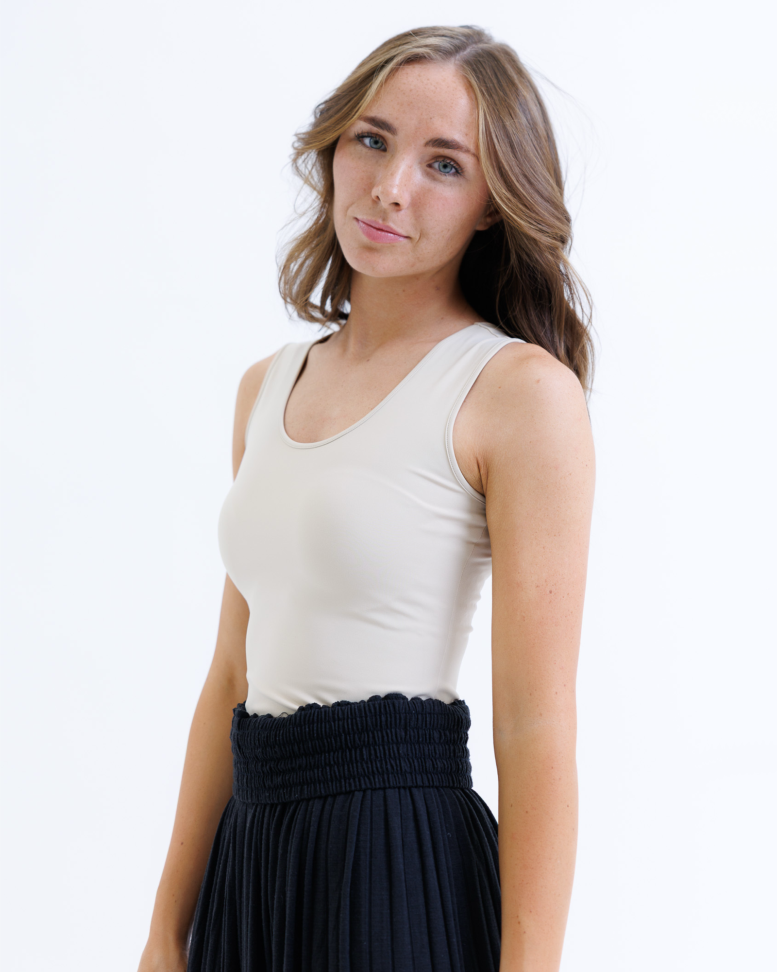 Woman wearing a nude layering tank top and black skirt on a white background