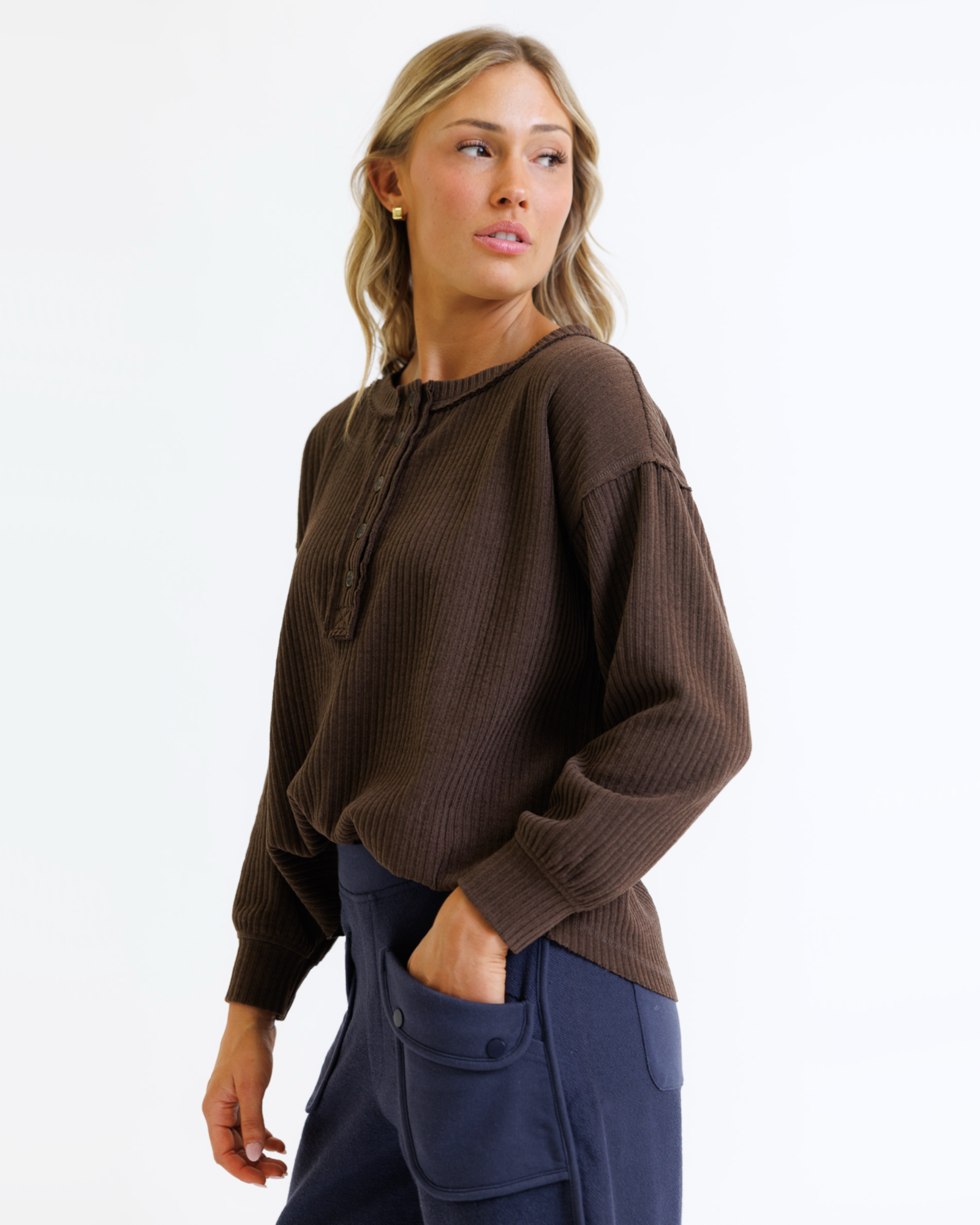 Woman wearing a brown long-sleeve top and navy pants on a white background